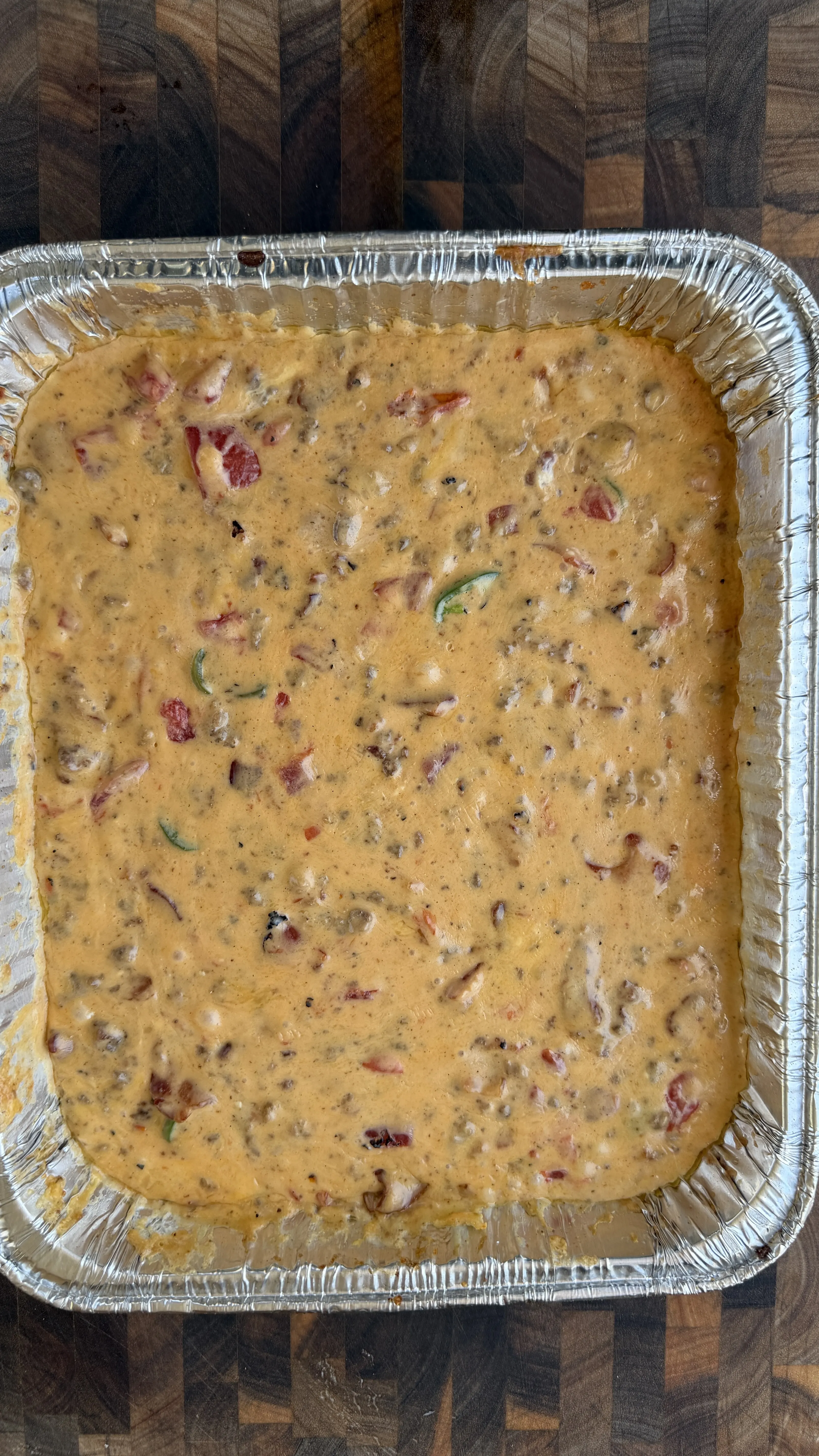Creamy smoked cheeseburger queso dip with tomatoes and jalapeños in a large aluminum foil pan