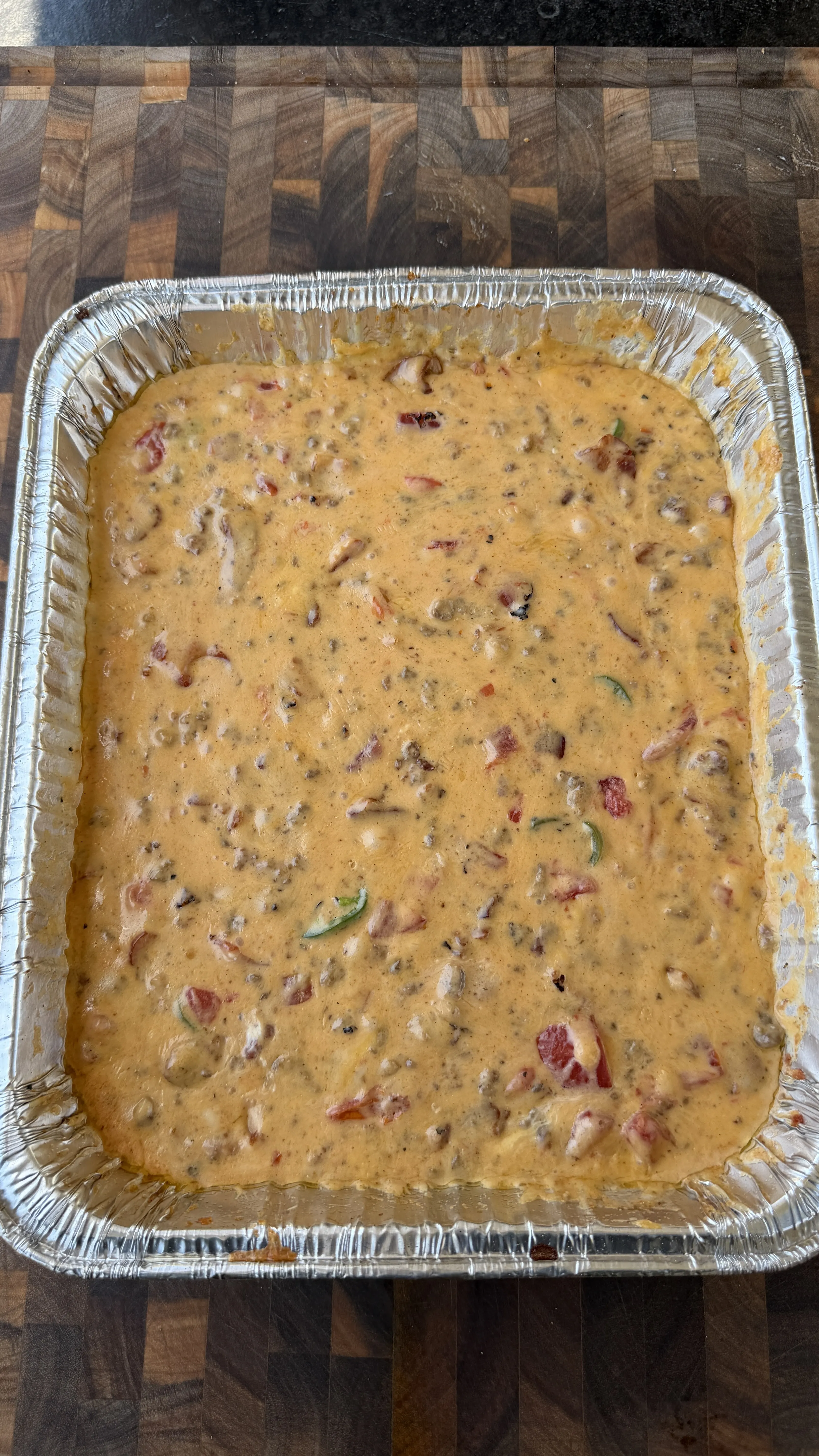 Creamy smoked cheeseburger queso dip with tomatoes and jalapeños in a large aluminum foil pan