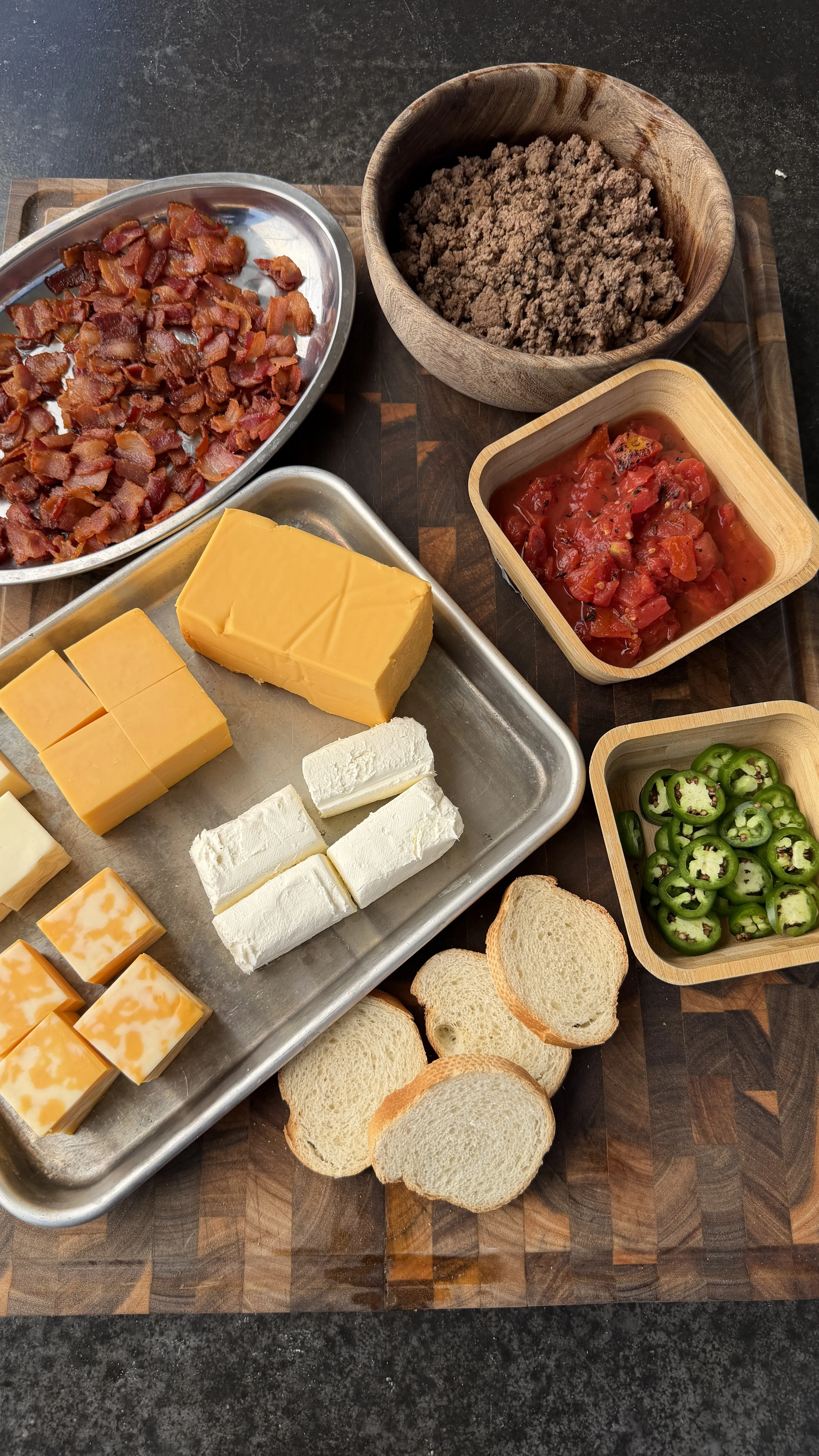 Ingredients for smoked cheeseburger queso dip: ground beef, bacon, cheddar, cream cheese, jalapeños, tomatoes, and bread