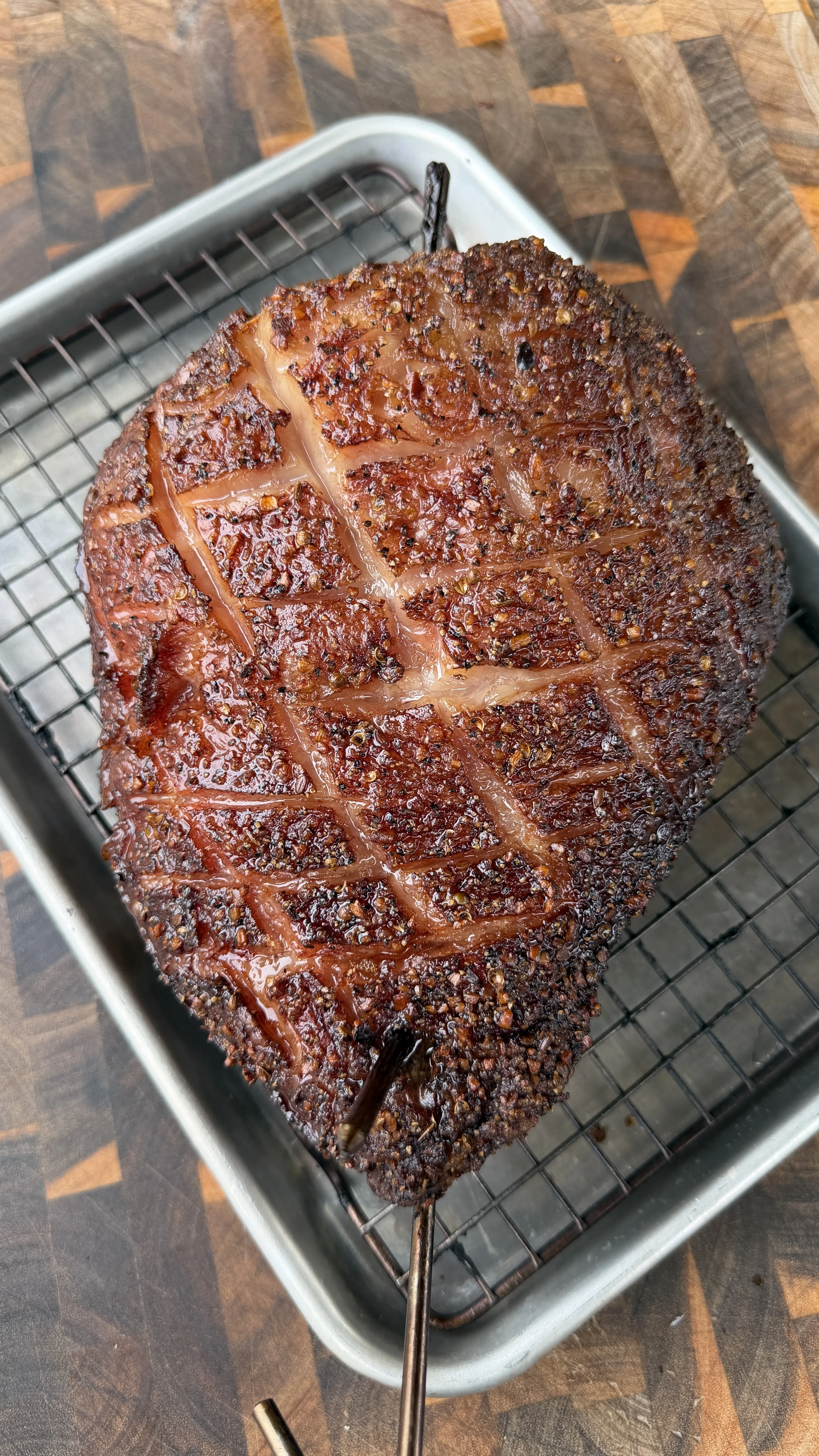Whole smoked picanha roast with score-marked fat cap on a wire rack in a roasting pan