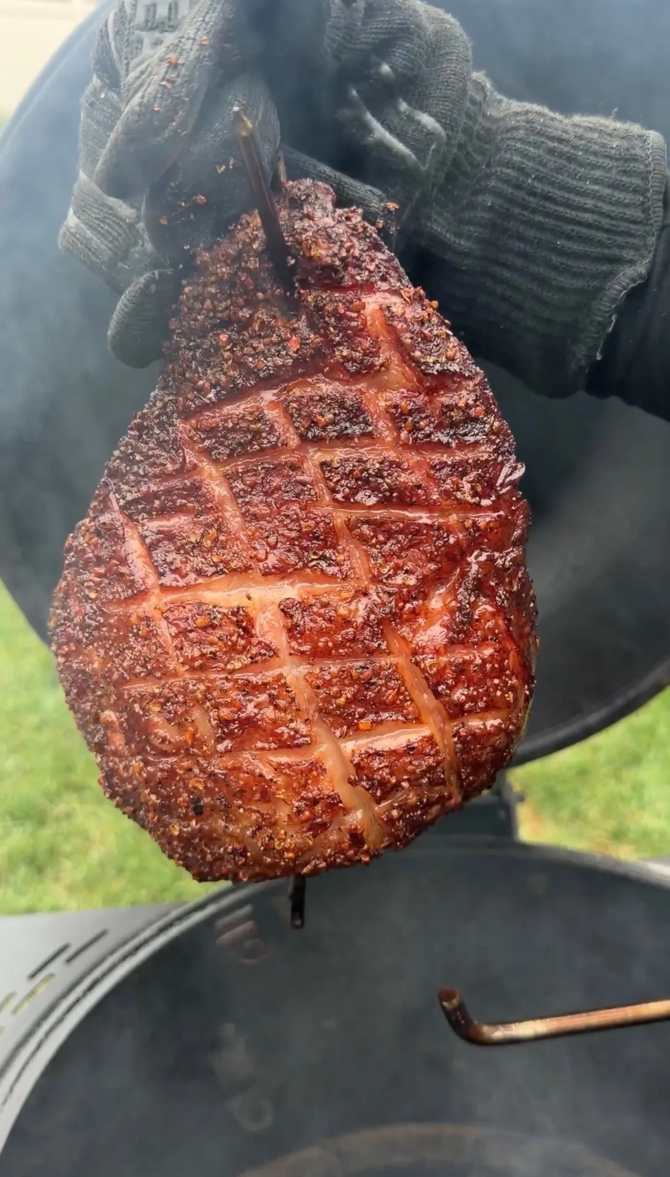 Smoked picanha roast with scored diamond-pattern fat cap, held over a smoker with rich mahogany bark