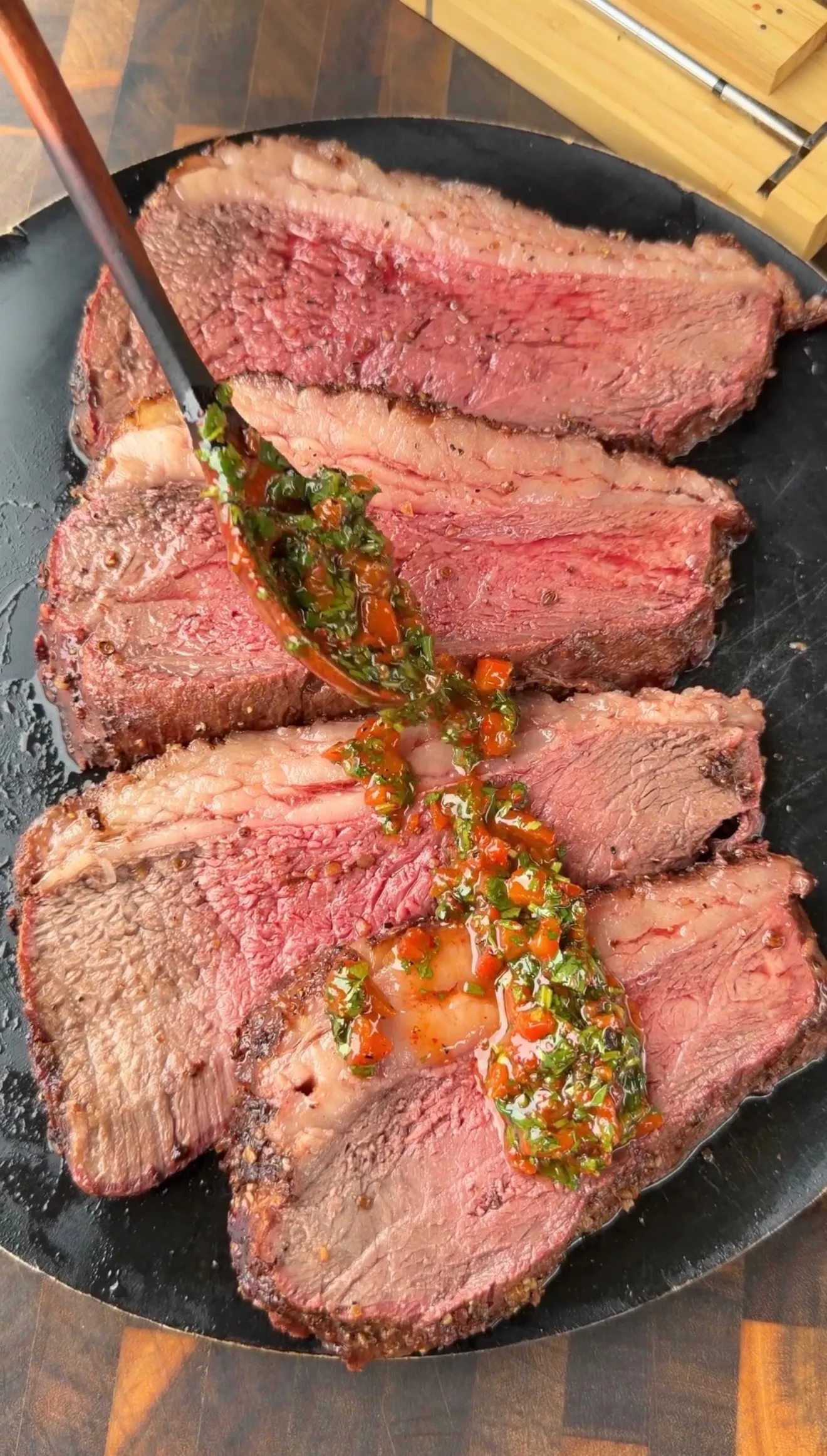 Sliced smoked picanha roast on black plate drizzled with red cilantro chimichurri sauce