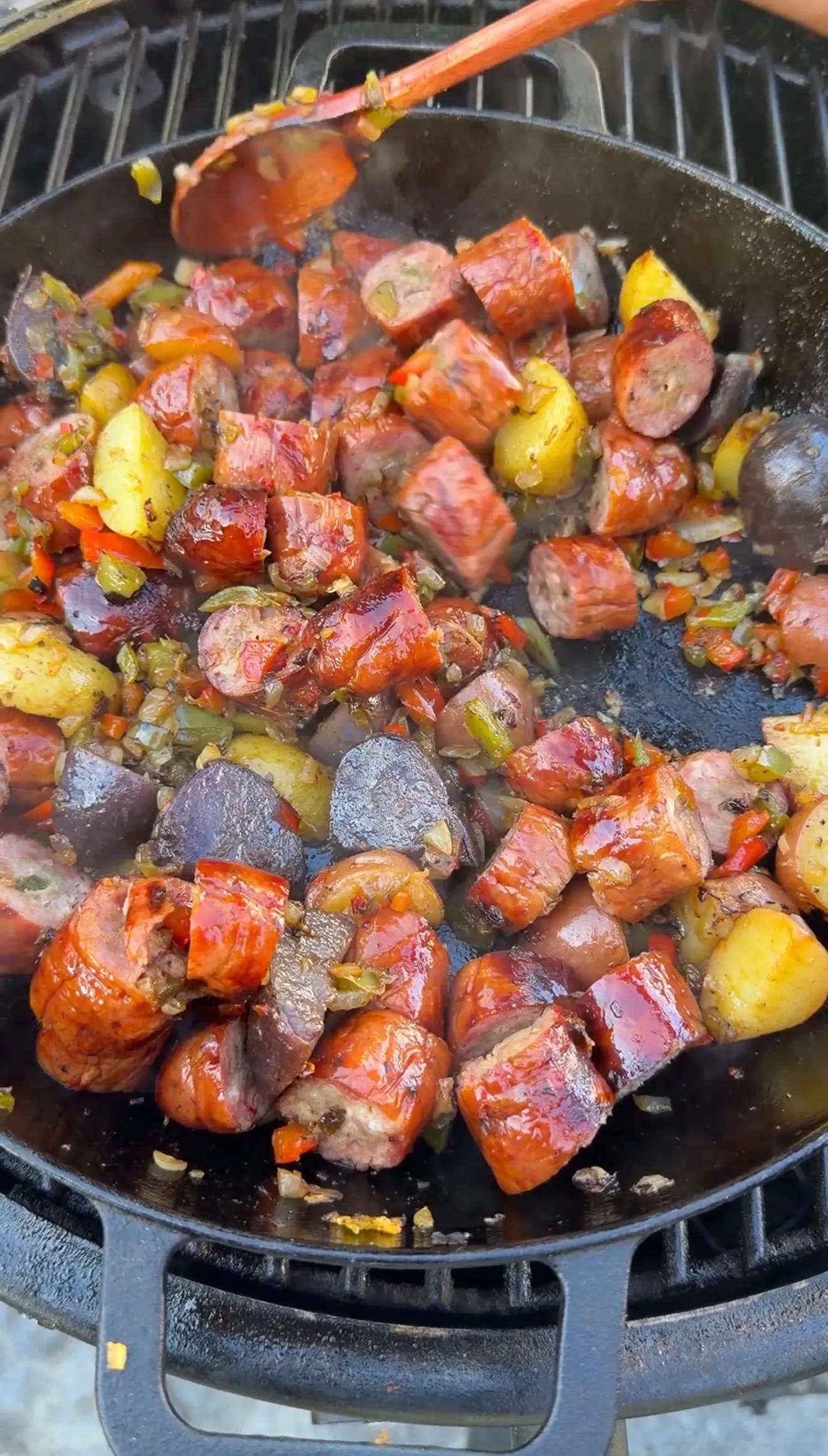Smoked sausage breakfast skillet with colorful potatoes and peppers cooking in a cast iron pan on a grill