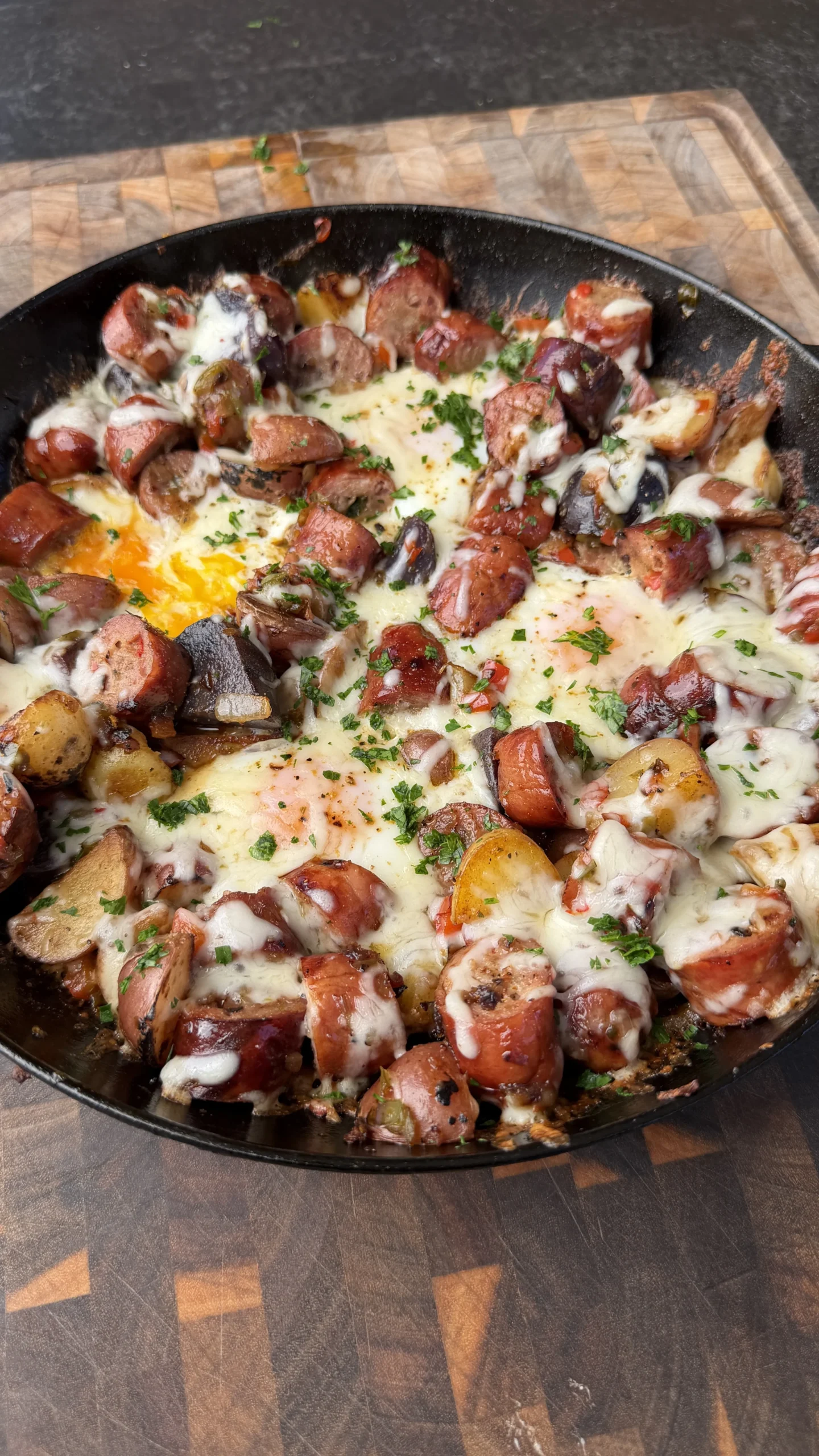 Cast iron skillet with smoked sausage, roasted potatoes, eggs, melted cheese, and fresh parsley garnish