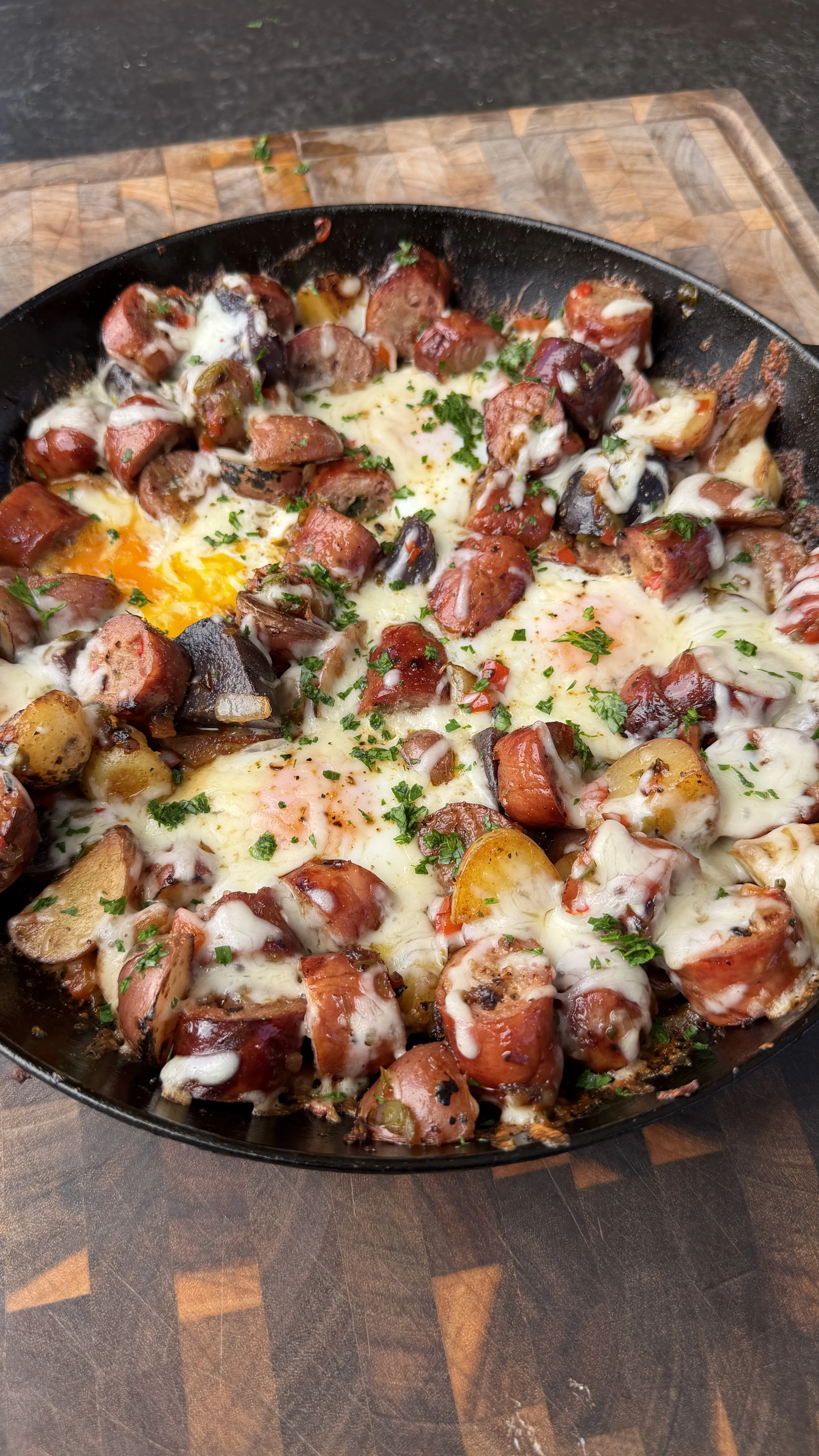 Cast iron skillet with smoked sausage, roasted potatoes, eggs, melted cheese, and fresh parsley garnish