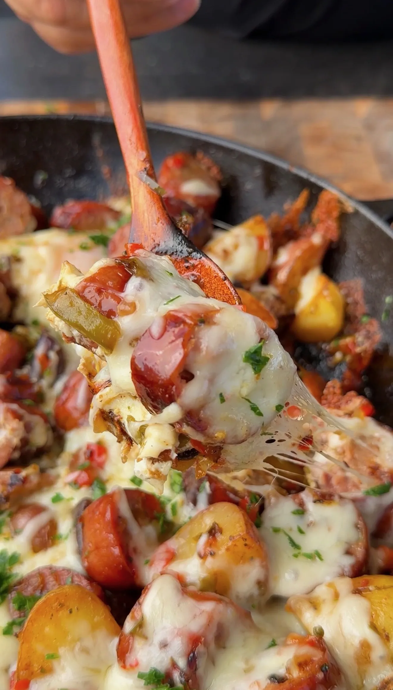 Cheesy smoked sausage breakfast skillet with potatoes, peppers, and melted mozzarella being served with a wooden spoon