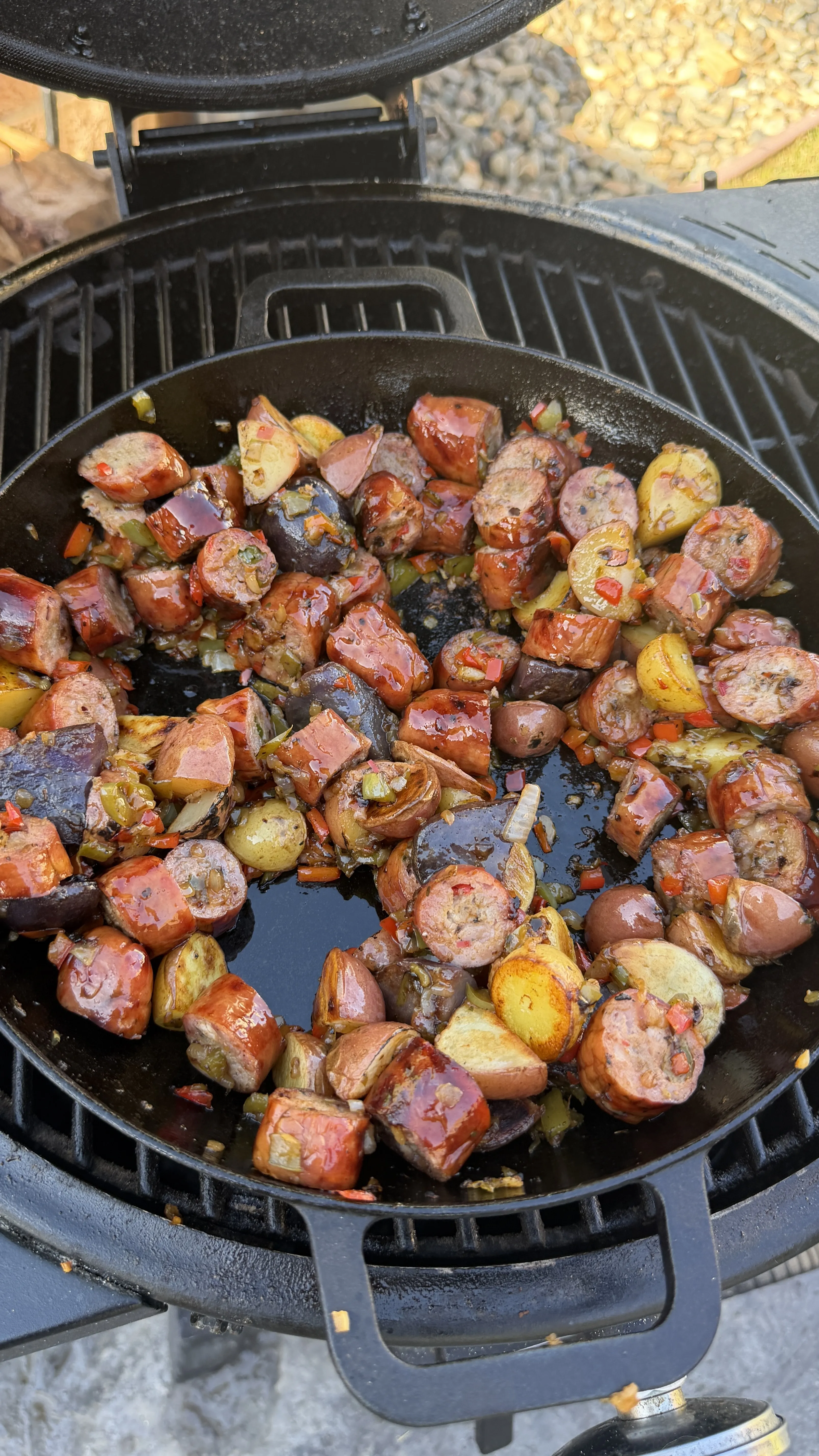 Cast iron skillet of diced potatoes with peppers cooking on a kamado grill for a breakfast skillet