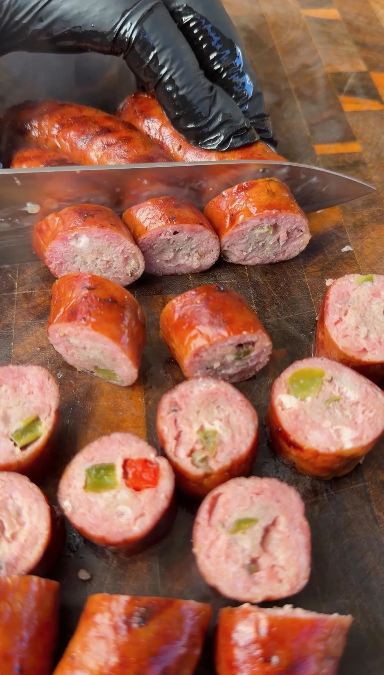 Sliced smoked sausage links stuffed with peppers and cheese on a dark wooden cutting board
