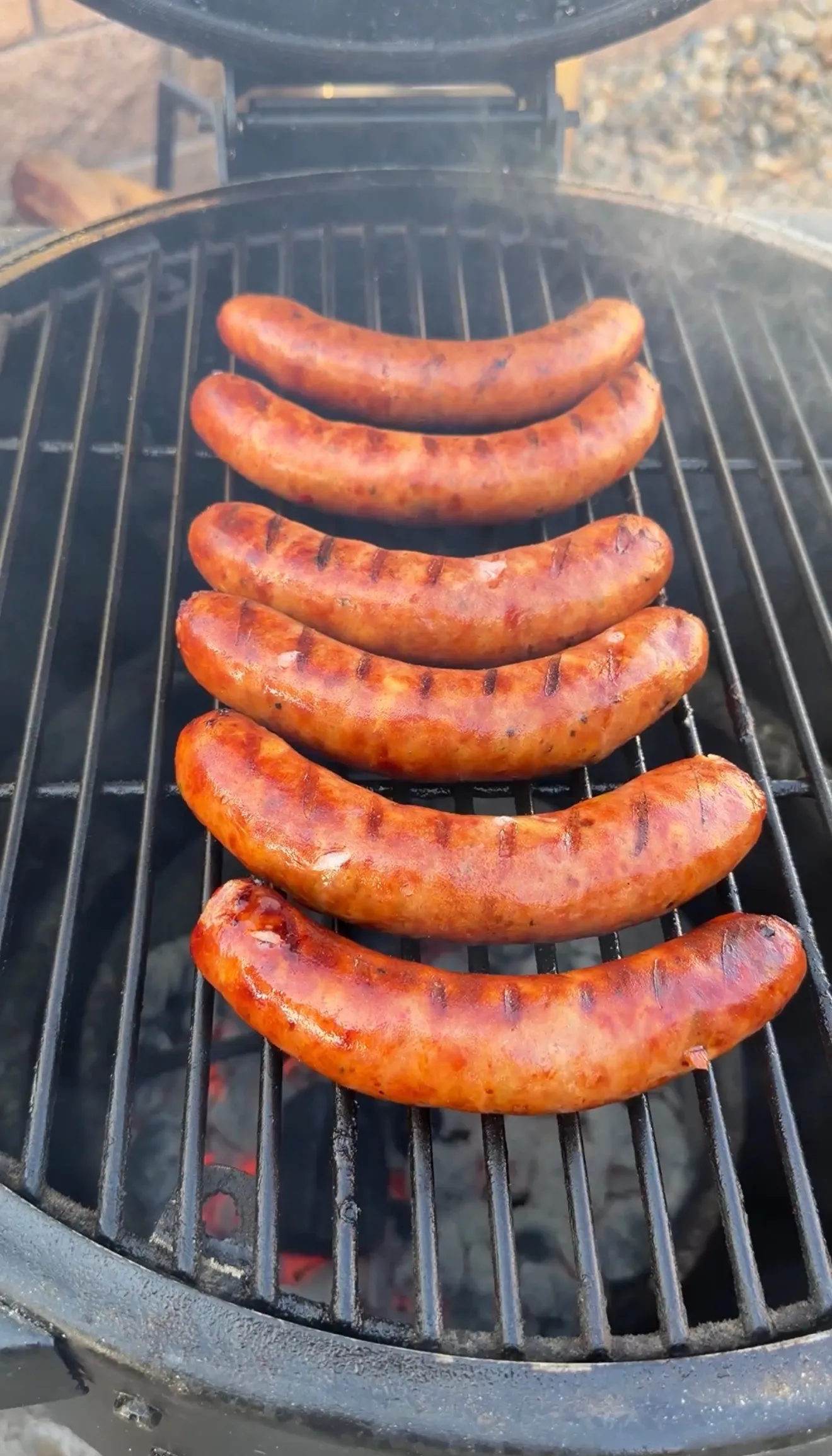 Seven smoked sausages with grill marks cooking over hot charcoal on a round kettle grill