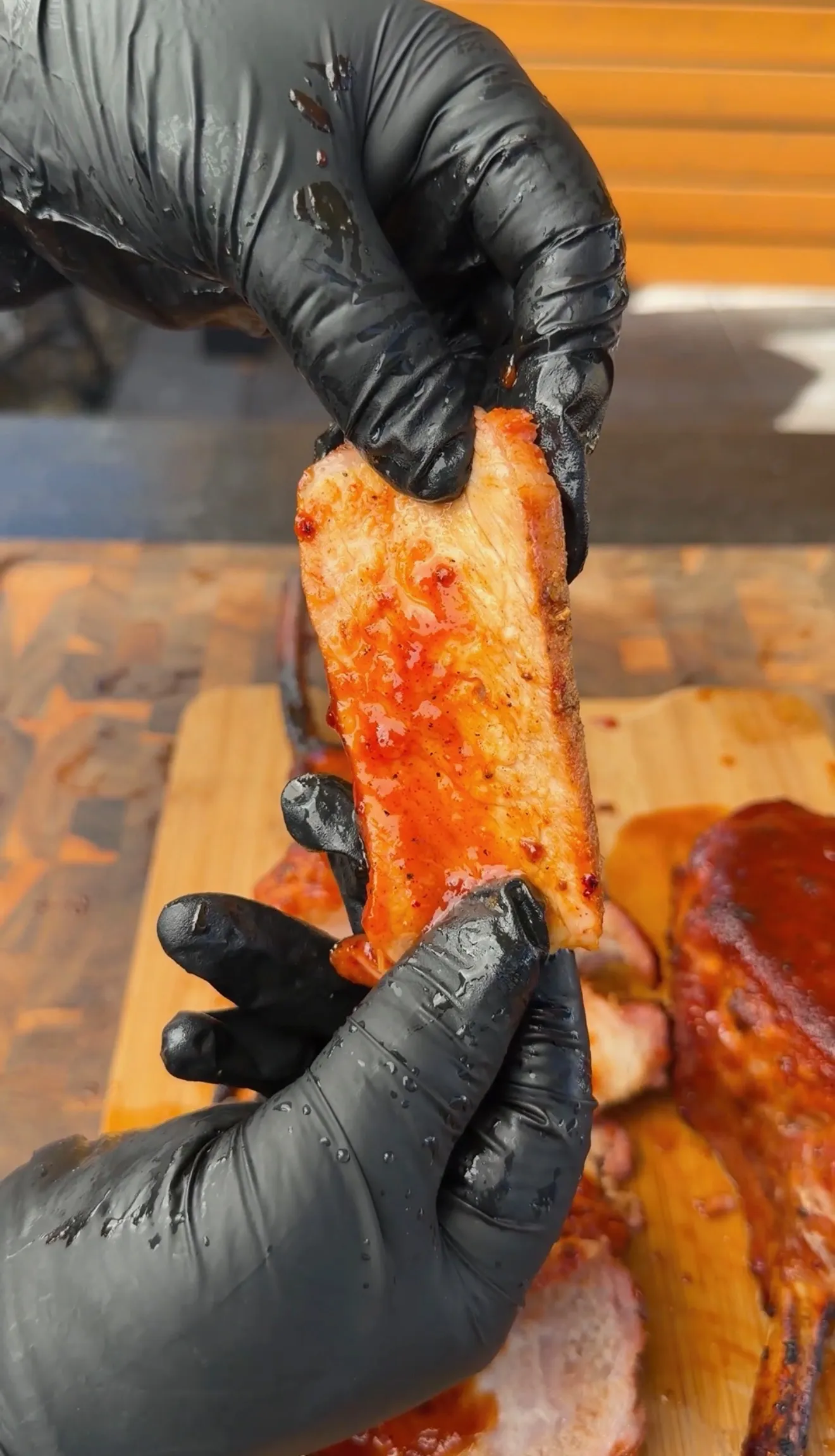 Gloved hands holding a glazed smoked tomahawk pork chop with sticky black raspberry BBQ sauce on a cutting board