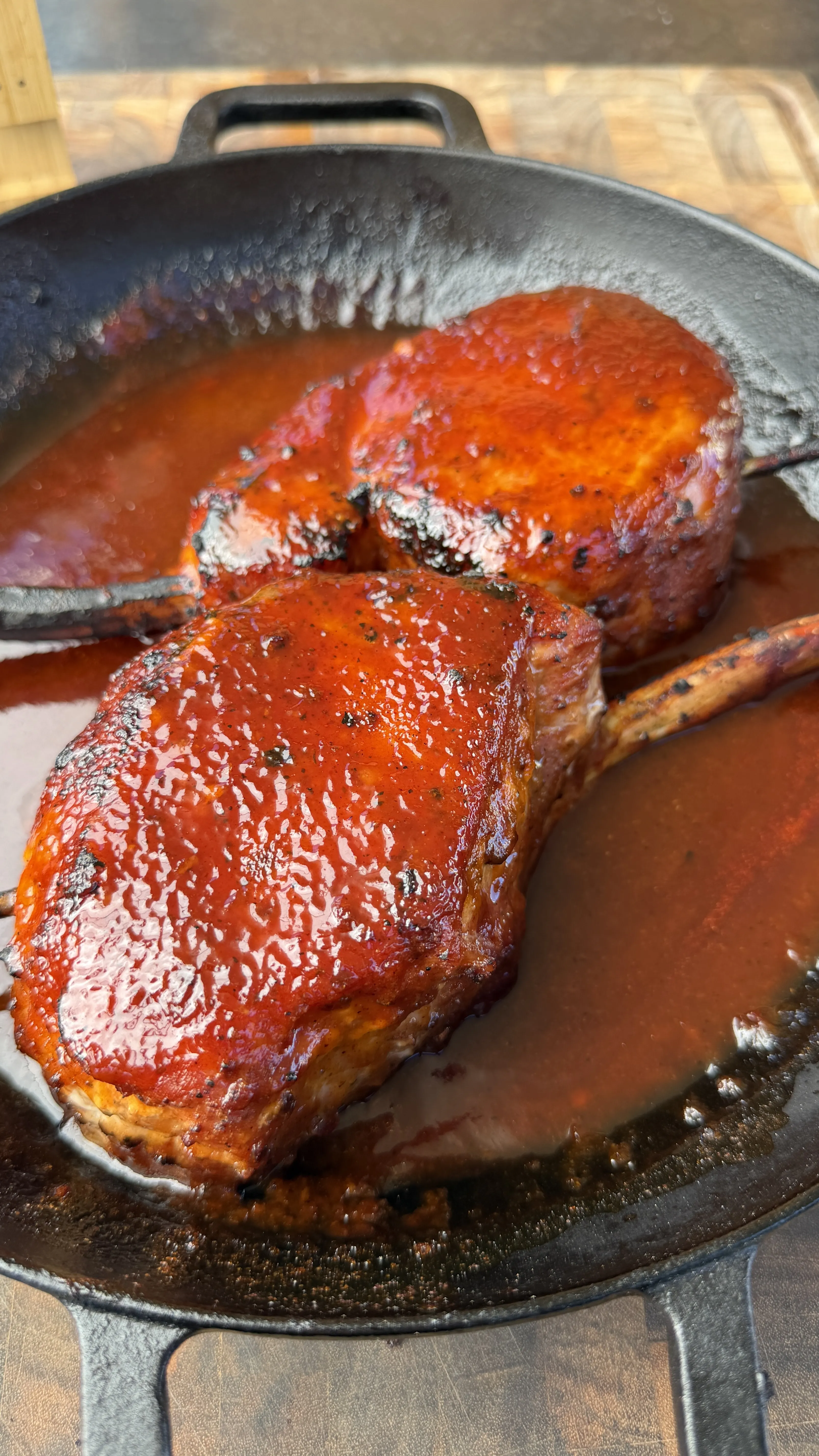Two glazed smoked tomahawk pork chops with black raspberry BBQ sauce simmering in a cast iron skillet