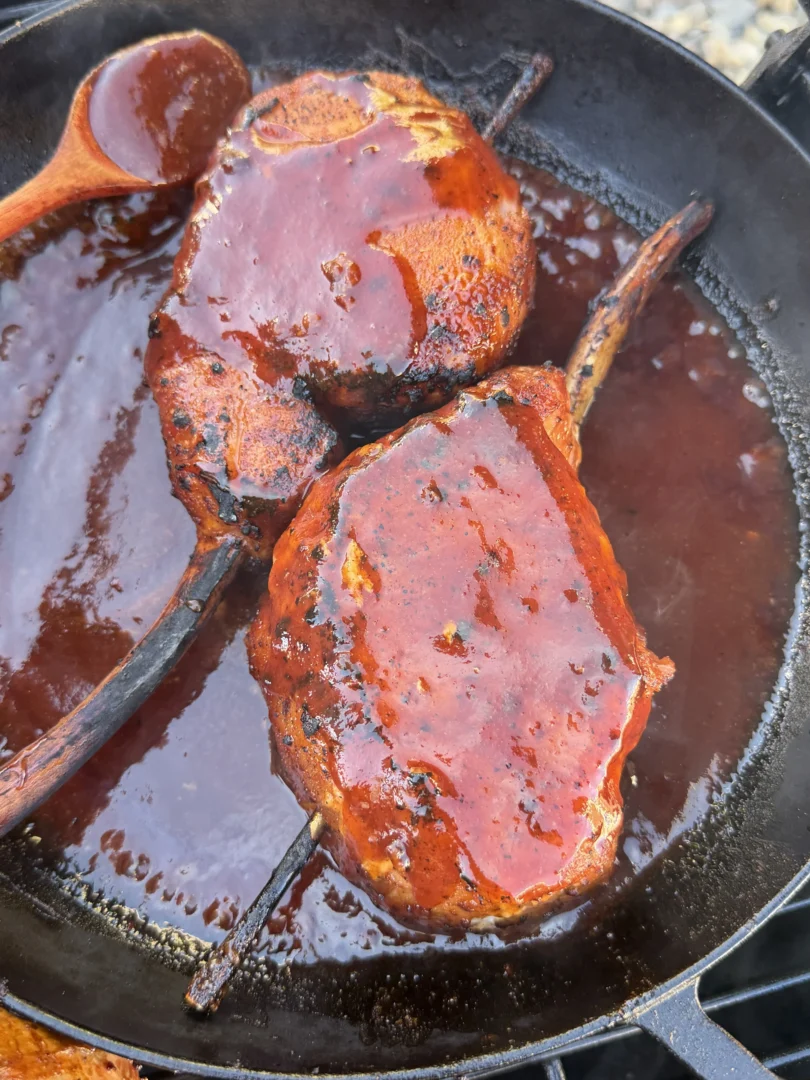 Smoked tomahawk pork chops glazed in black raspberry BBQ sauce simmering in a cast iron skillet