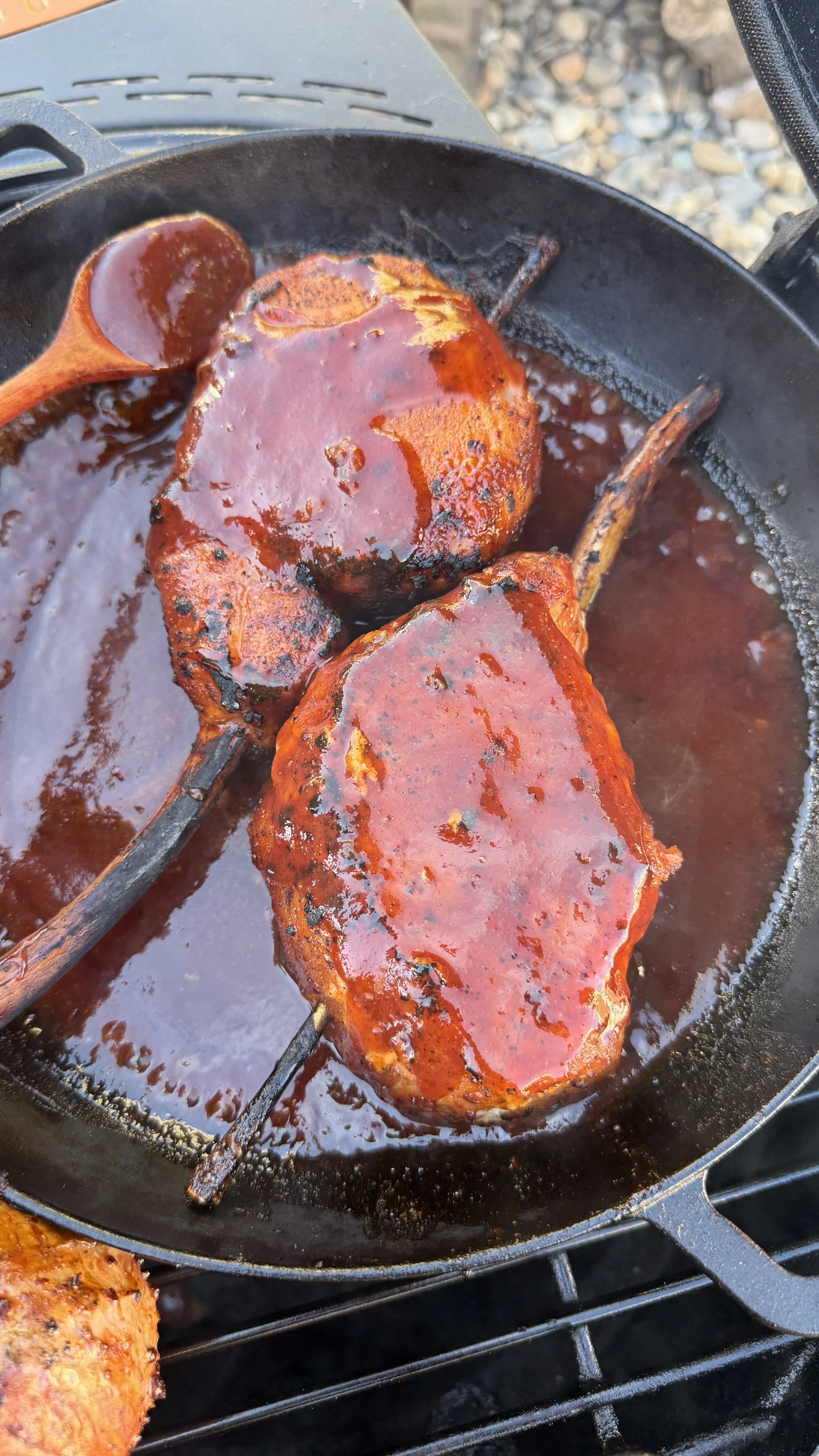 Smoked tomahawk pork chops glazed in black raspberry BBQ sauce simmering in a cast iron skillet