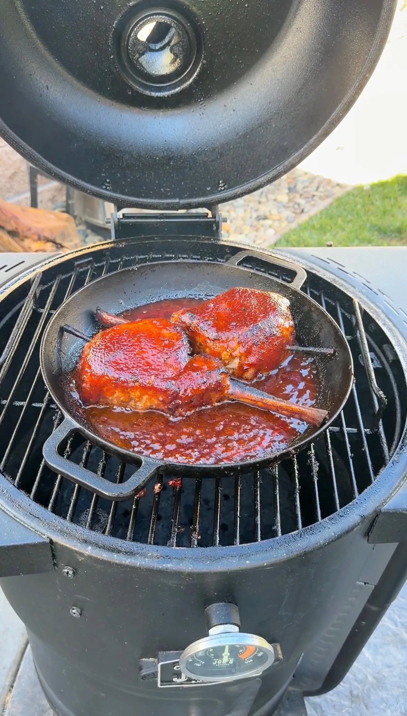 Tomahawk pork chops glazed in black raspberry BBQ sauce cooking in a cast iron skillet on a kamado grill