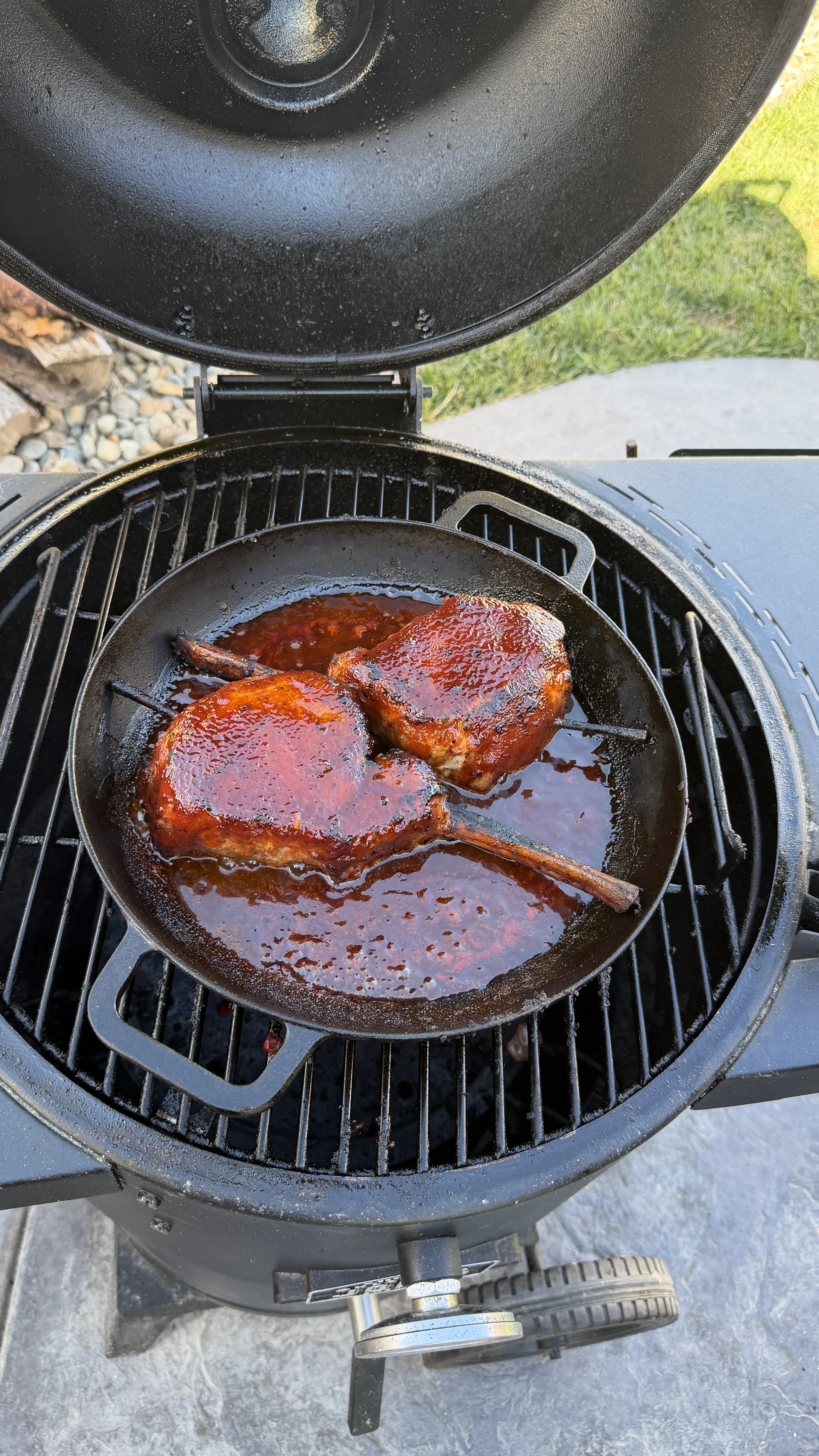 Two glazed black raspberry BBQ tomahawk pork chops sizzling in a cast iron skillet on a ceramic grill