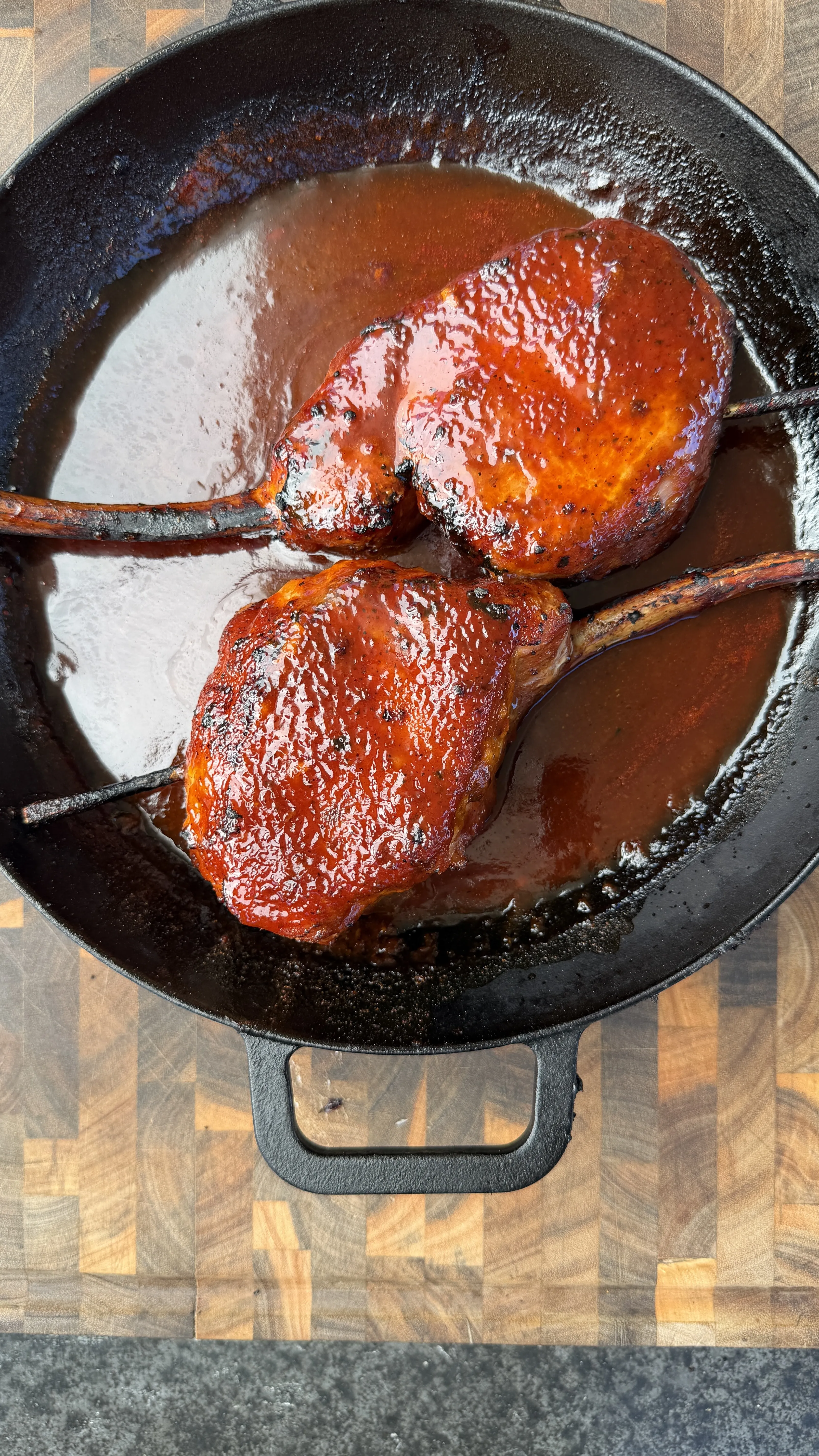 Two glazed smoked black raspberry BBQ tomahawk pork chops in a cast iron skillet with rich sauce