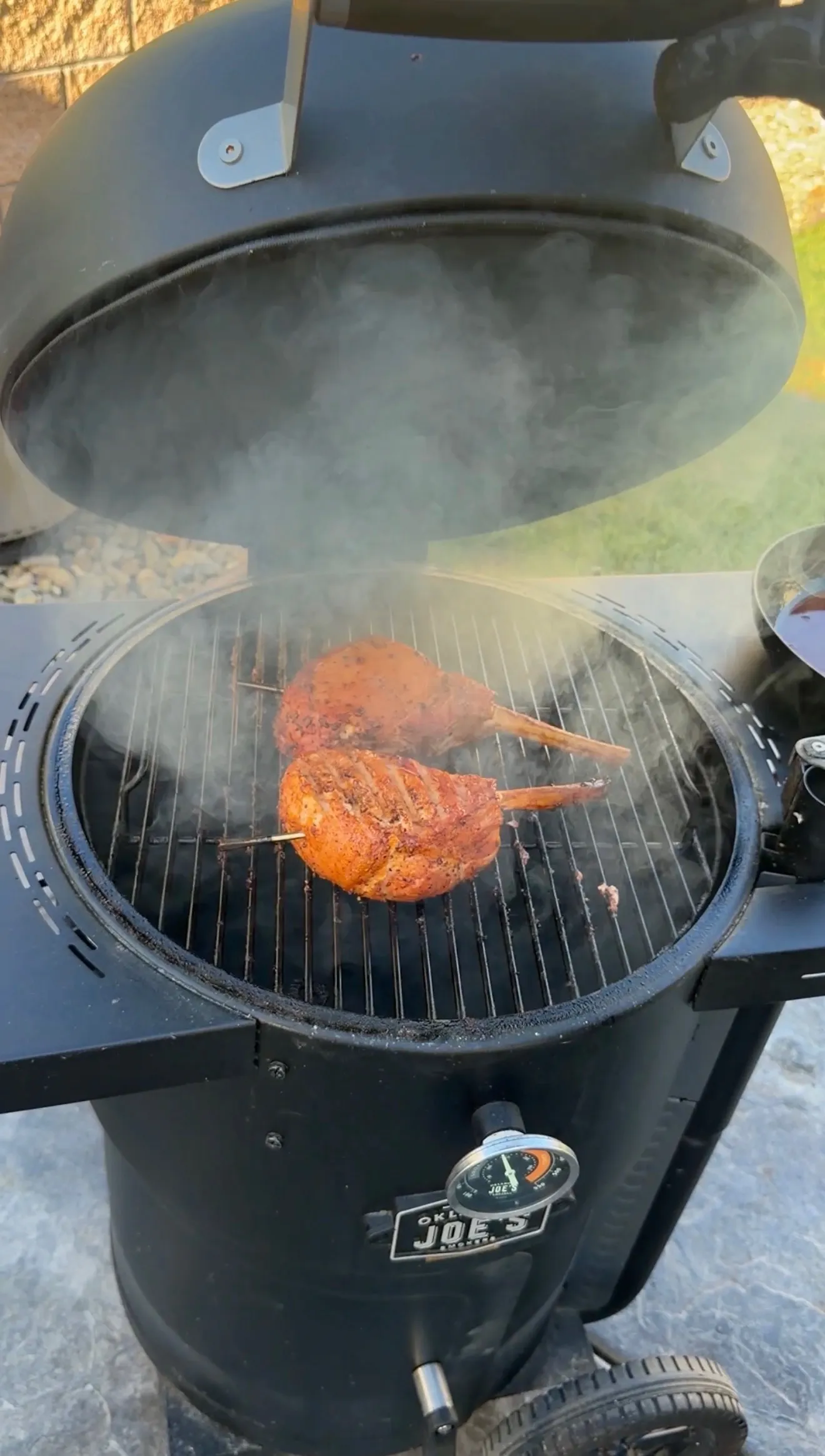Two smoked tomahawk pork chops with black raspberry BBQ rub smoking on an Oklahoma Joe's charcoal grill