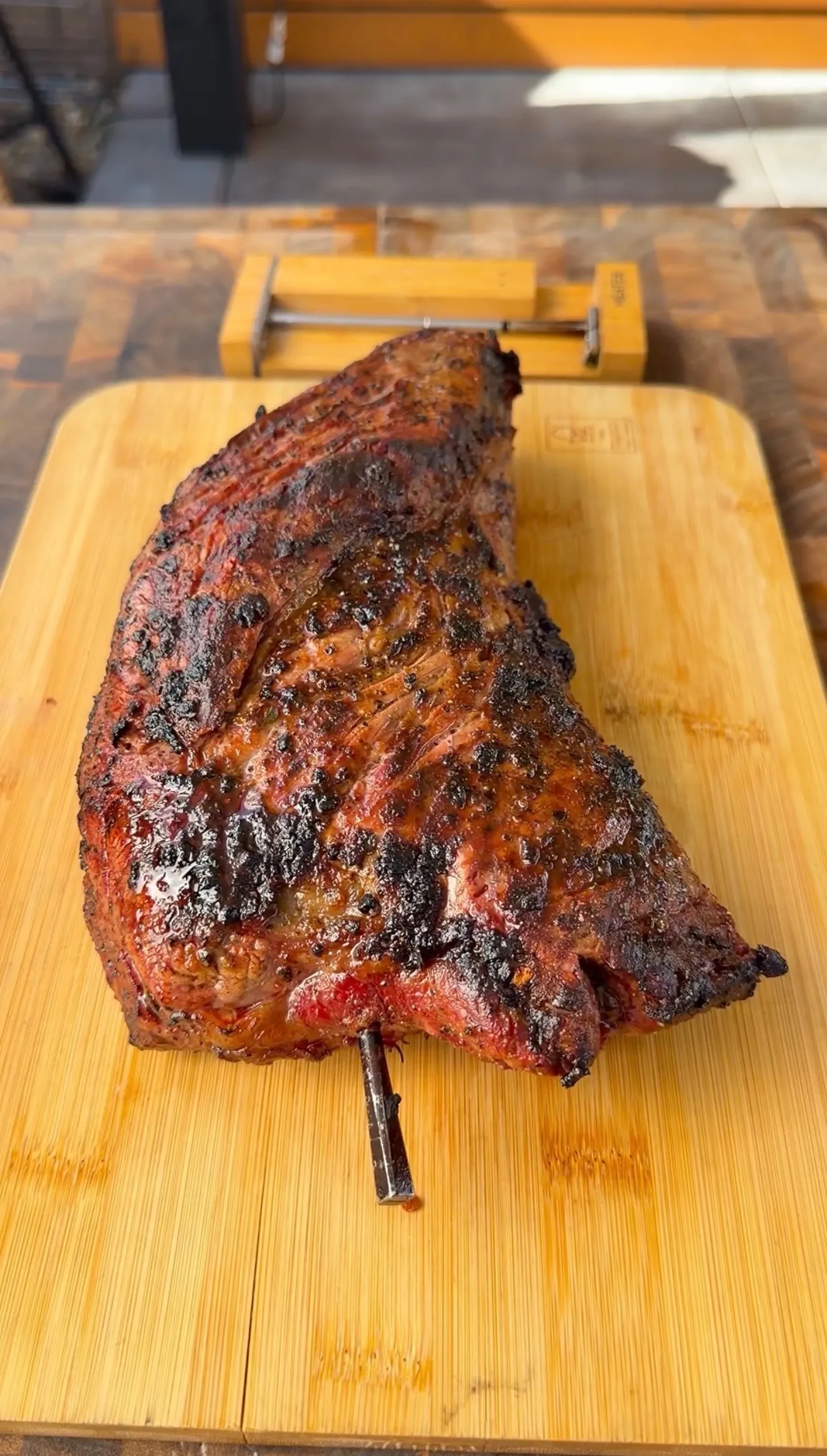 Whole smoked tri-tip with dark bark crust resting on a bamboo cutting board, bone exposed