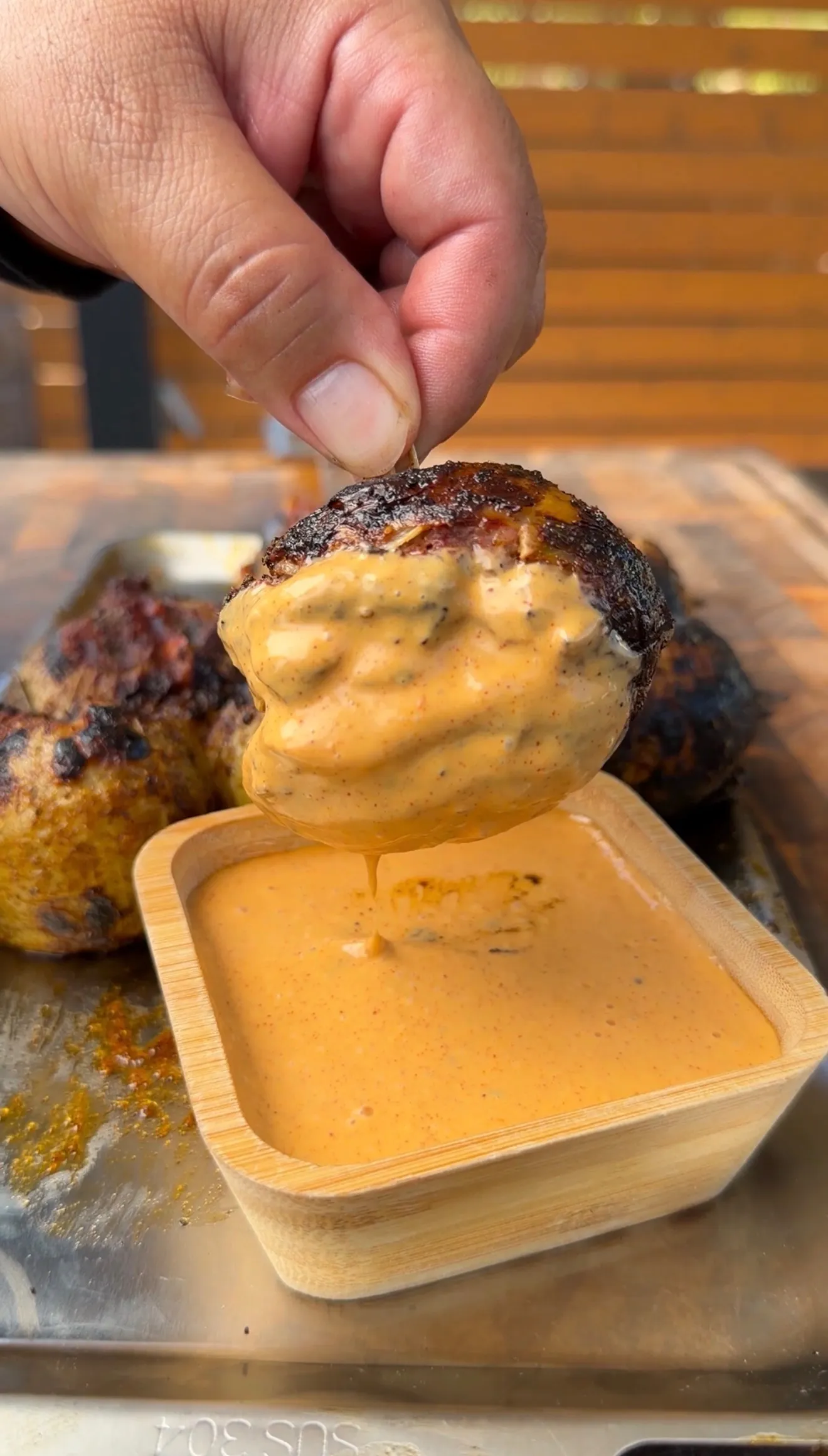 Hand dipping a grilled stuffed onion bomb into a creamy chipotle dipping sauce in a wooden bowl