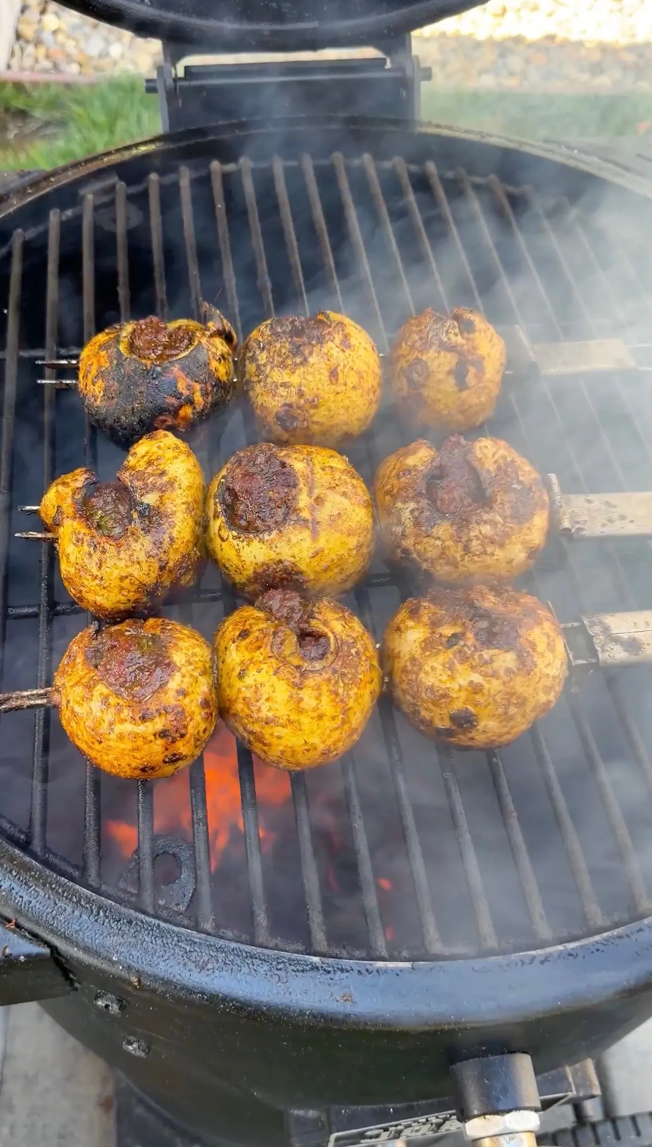 Nine spiced stuffed onion bombs on skewers grilling over hot coals with smoke rising