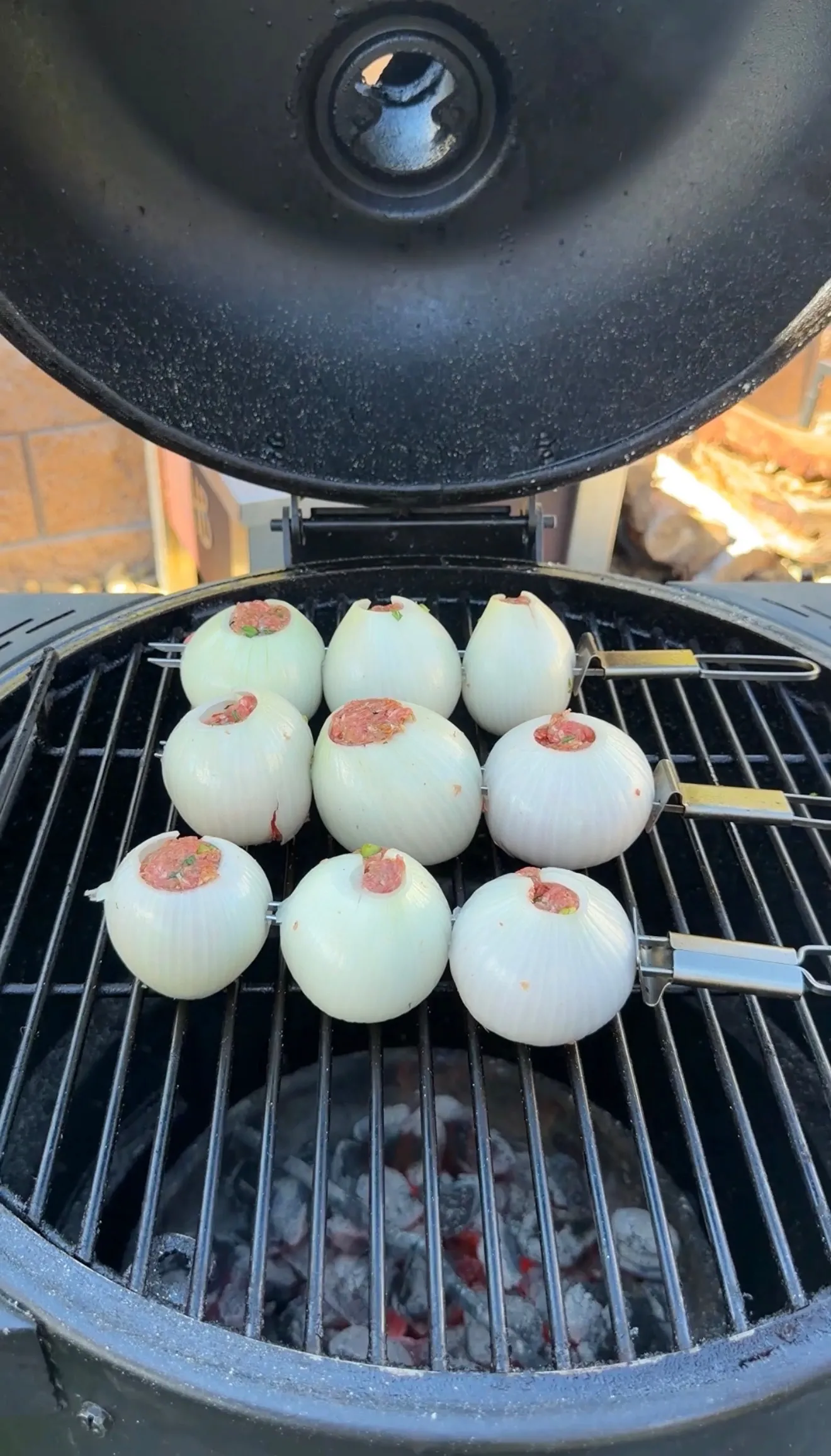 Nine whole white onions stuffed with seasoned meat mixture arranged on a round charcoal grill grate