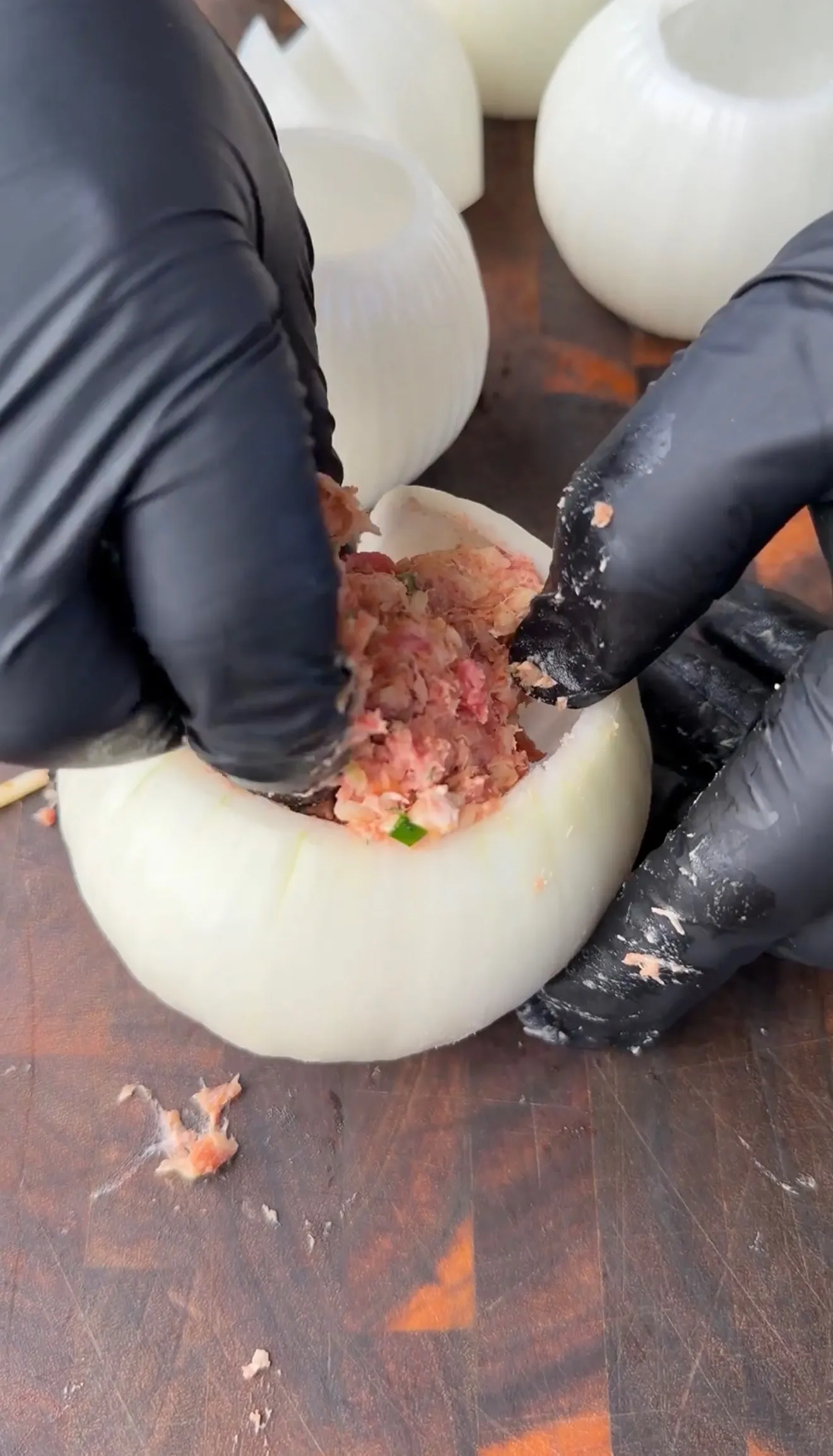 Gloved hands stuffing a hollowed white onion with seasoned ground meat mixture for onion bombs
