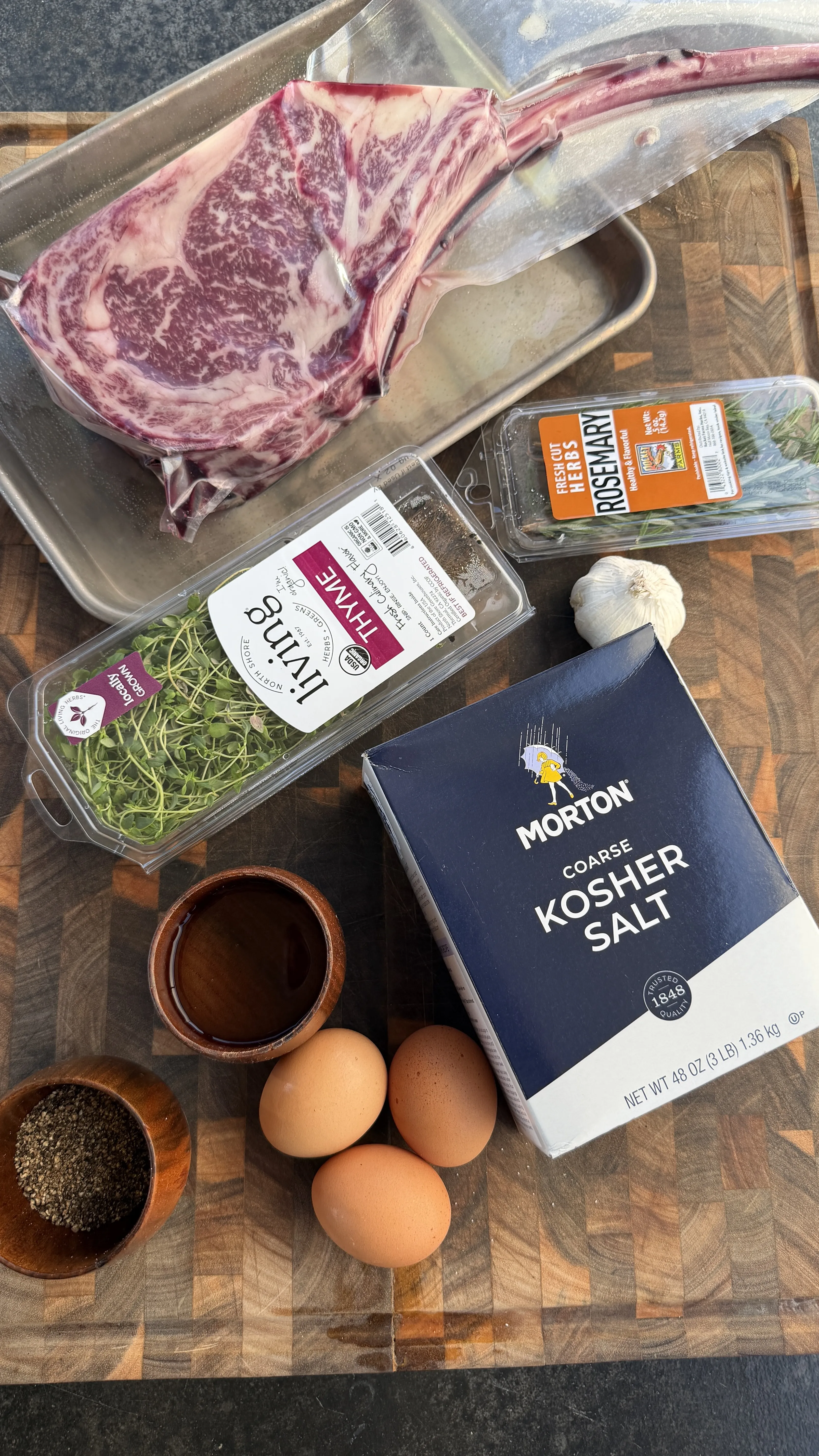 Raw tomahawk ribeye steak with kosher salt, egg whites, thyme, rosemary, garlic, and black pepper on a wooden board