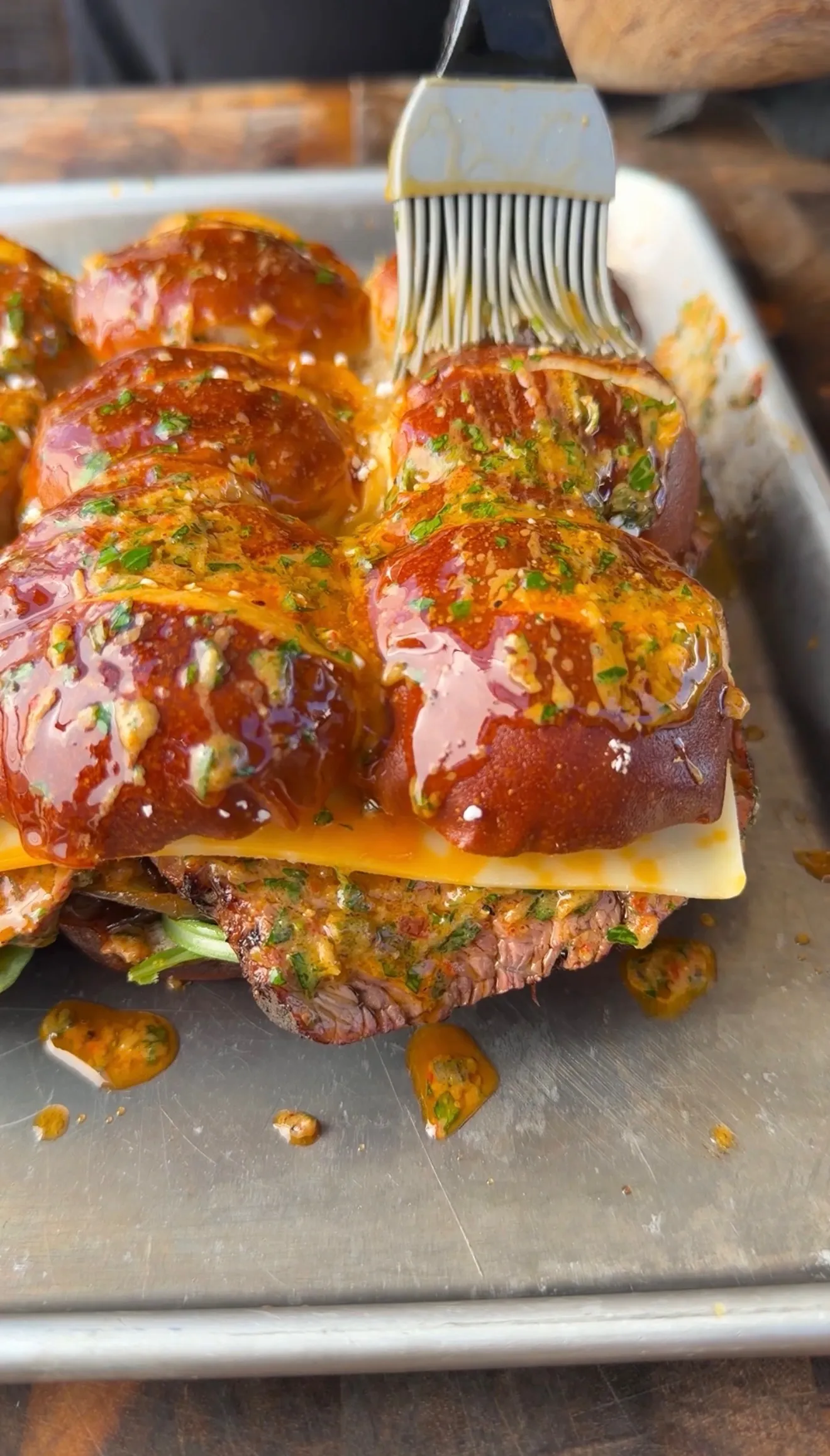 Tri-tip cowboy butter sliders on a baking sheet being brushed with herbed butter sauce over pretzel buns