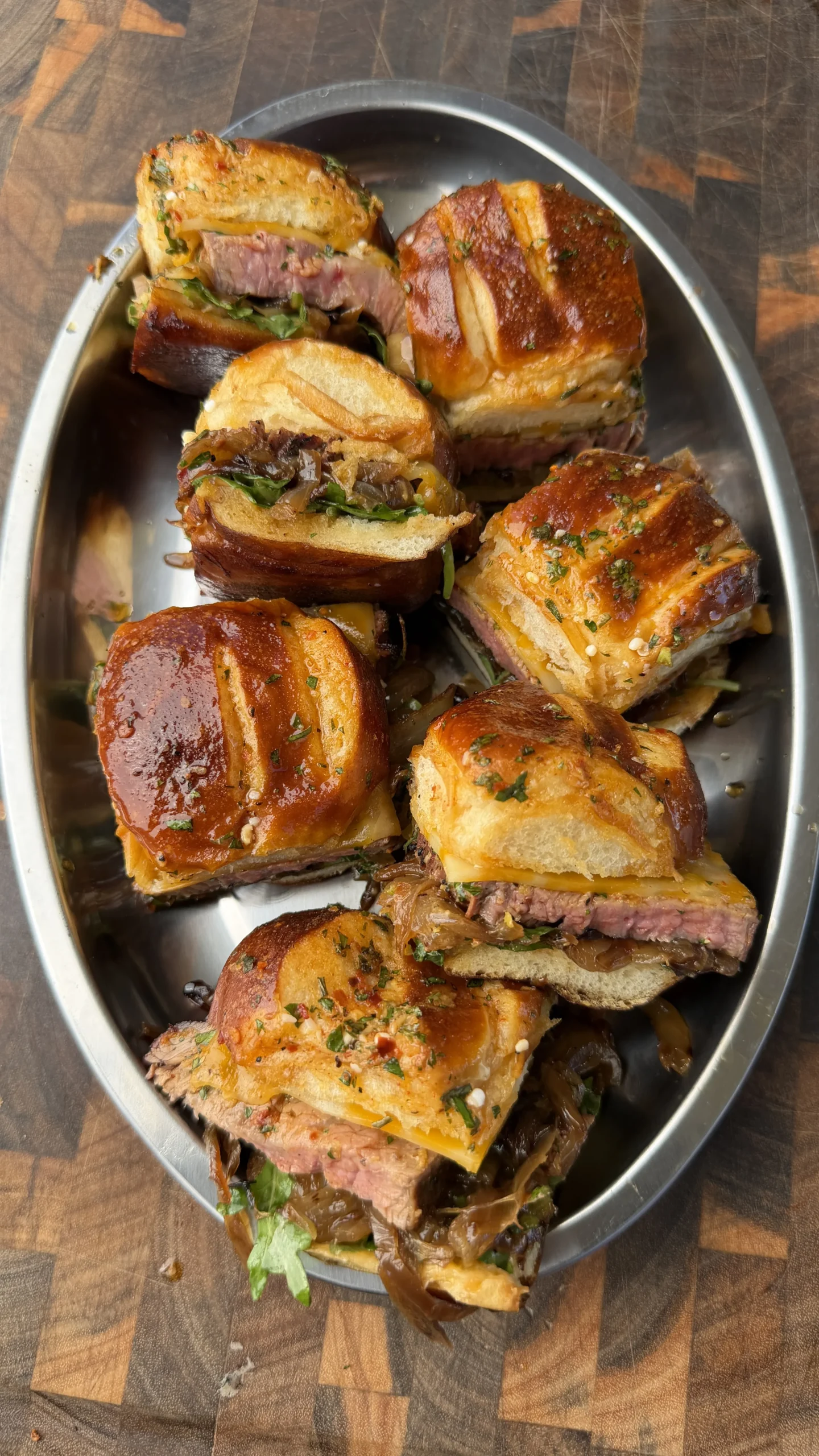 Tri-tip cowboy butter sliders piled on a silver oval platter, showing juicy beef, melted cheese, and herb-glazed buns