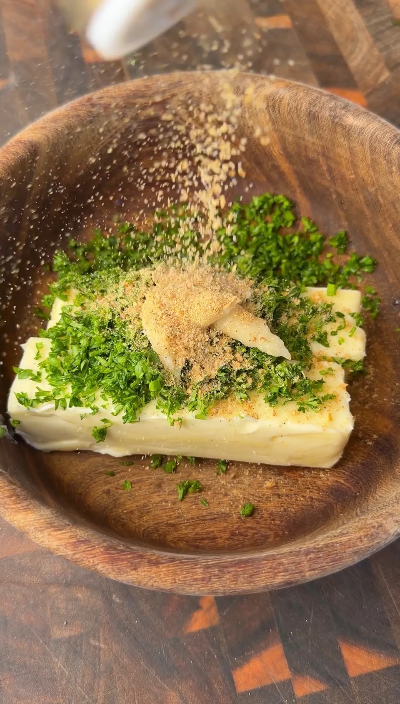 Stick of butter topped with fresh chopped parsley and garlic powder in a rustic wooden bowl for umami compound butter