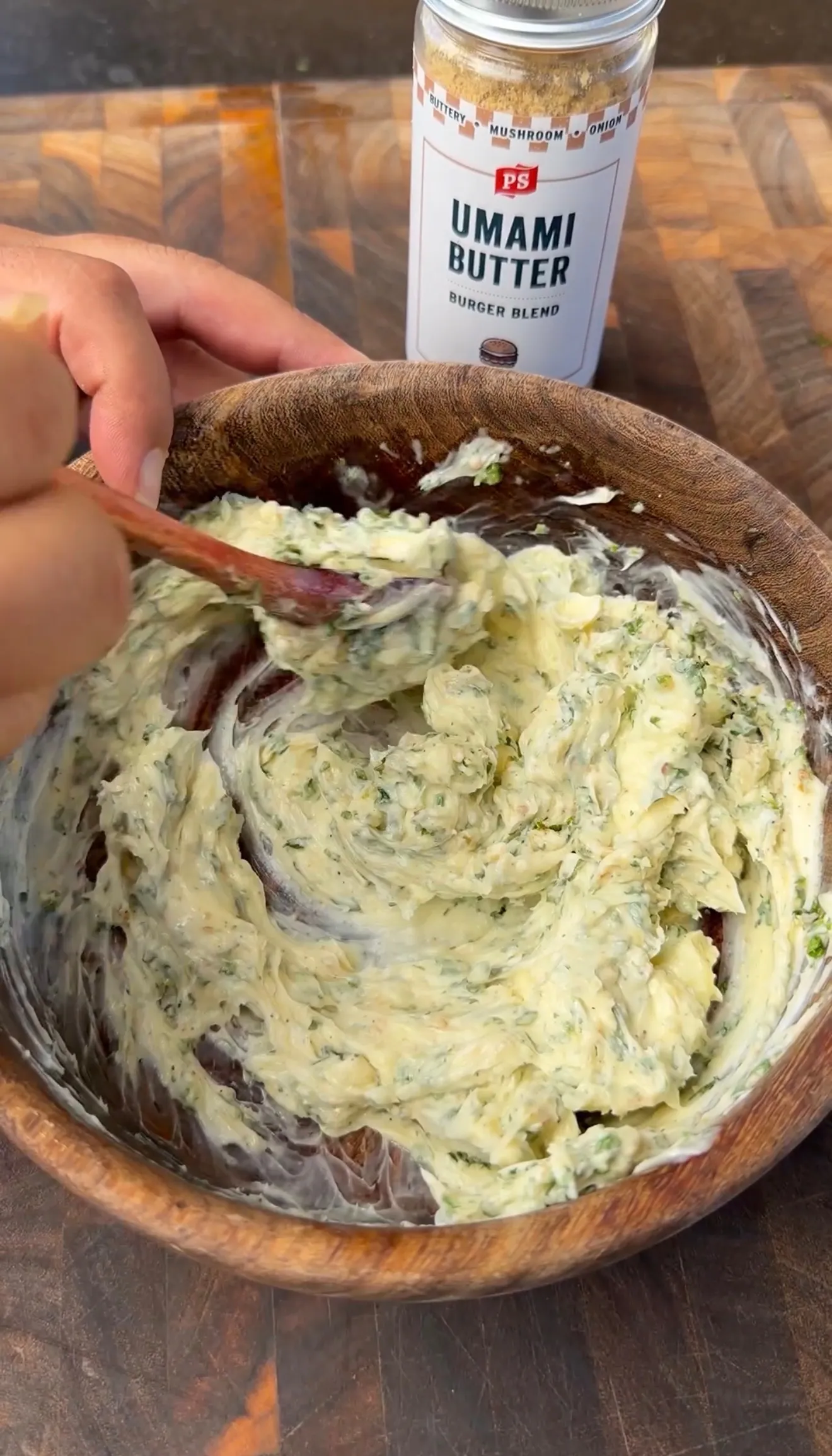 Herb compound butter being mixed in a wooden bowl with PS Umami Butter Burger Blend seasoning in background
