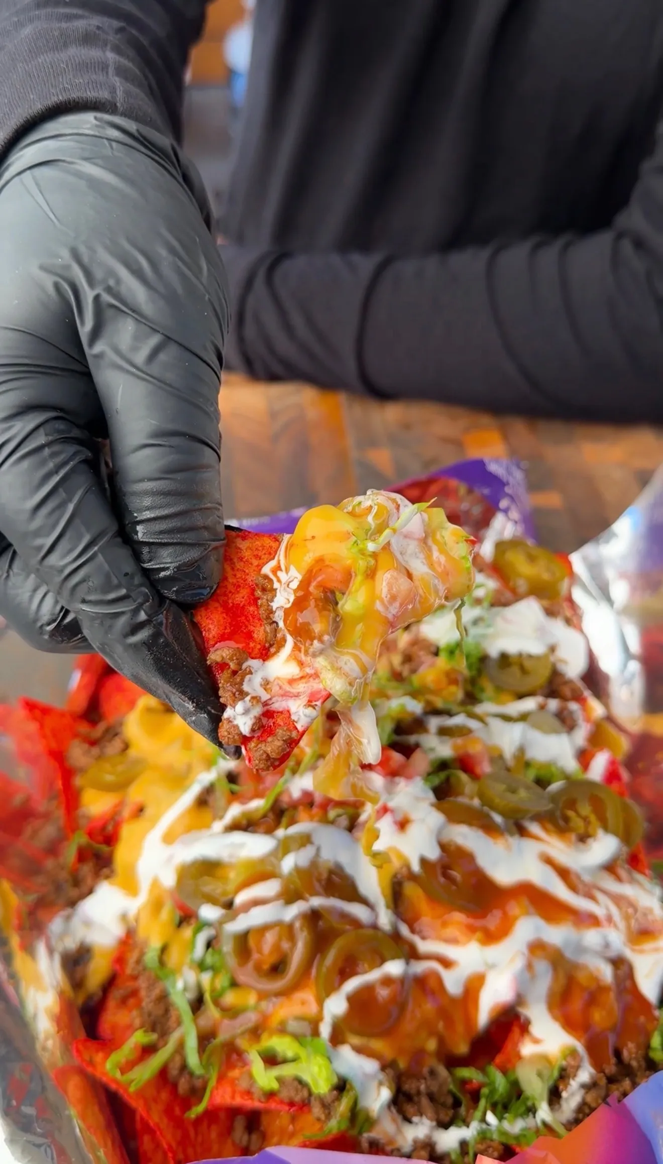 Gloved hand holding a Flamin' Hot Cheetos walking taco loaded with meat, cheese, sour cream, jalapeños, and lettuce