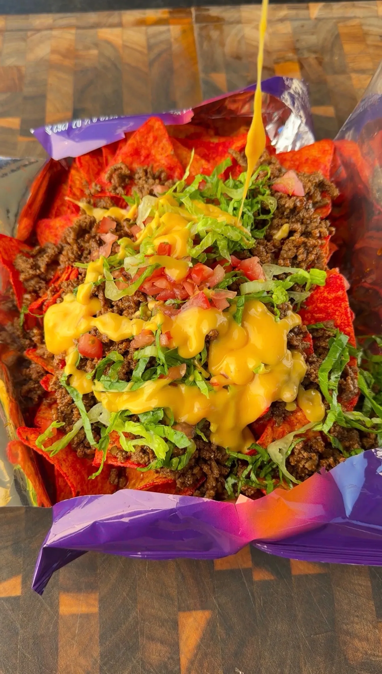Walking tacos served in an open Doritos bag topped with seasoned ground beef, shredded lettuce, tomatoes, and nacho cheese sauce