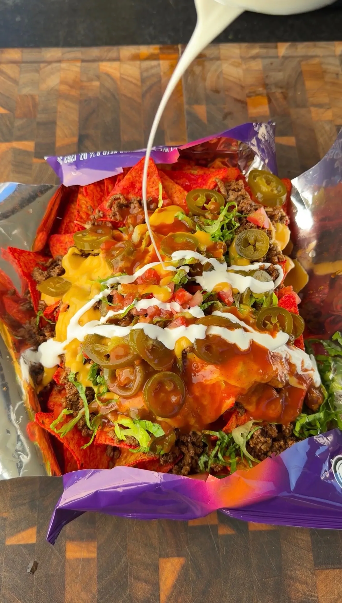 Walking tacos in an open Takis bag topped with seasoned beef, jalapeños, cheese sauce, salsa, and sour cream drizzle