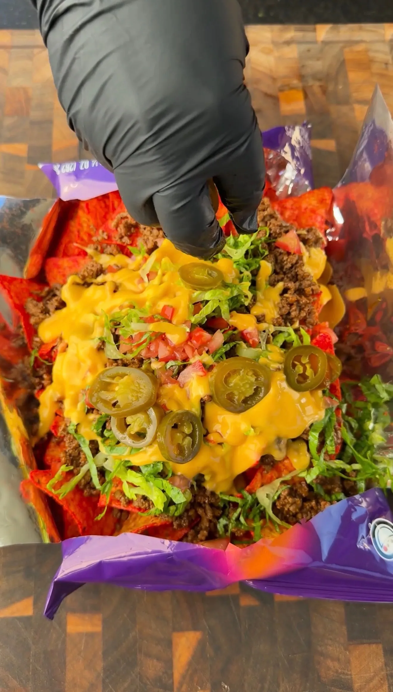 Walking tacos in an open chip bag topped with cheese sauce, seasoned beef, jalapeños, lettuce, and tomatoes
