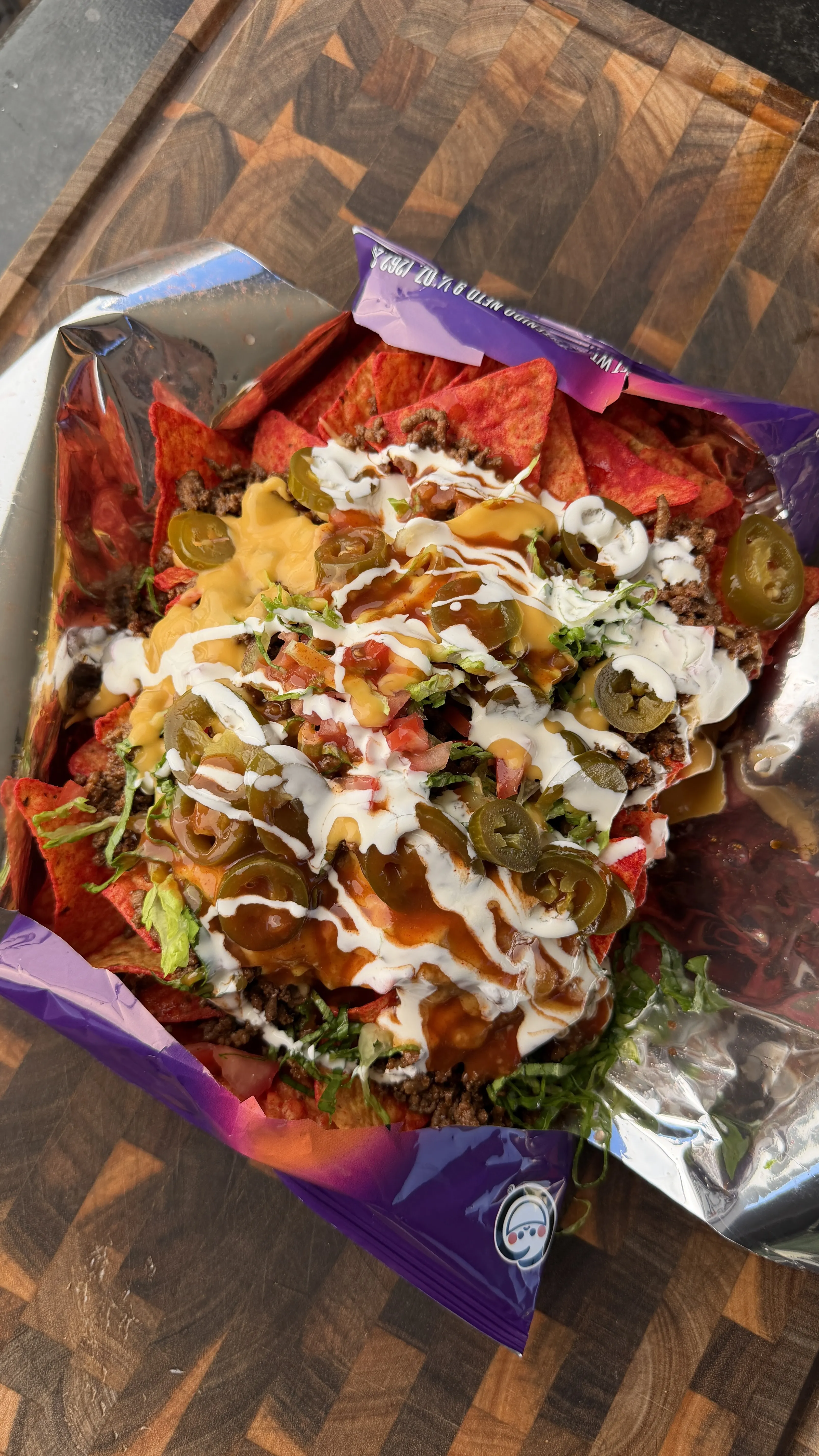 Walking tacos served in an open chip bag topped with seasoned beef, cheese sauce, sour cream, jalapeños, and lettuce