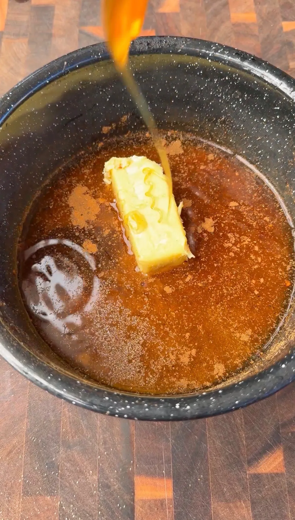 Stick of butter melting into apple cider glaze in a dark slow cooker for smoked St. Louis spare ribs