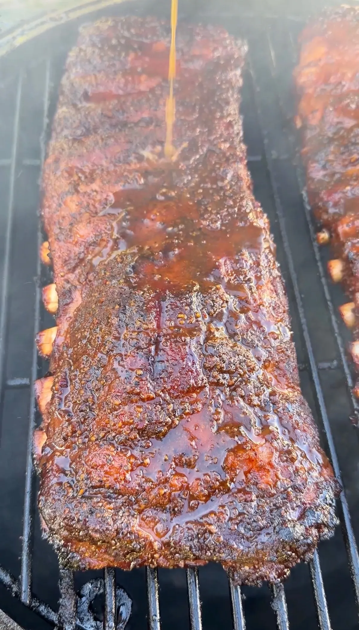 Apple cider glazed St. Louis spare ribs being sauced on smoker grill with caramelized BBQ crust
