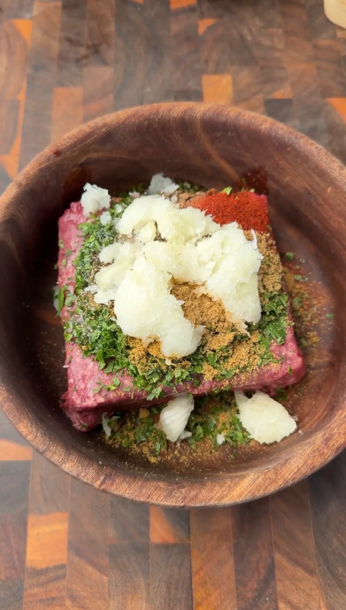 Ground beef with grated onion, parsley, cumin, coriander, smoked paprika, allspice, and garlic in a wooden bowl