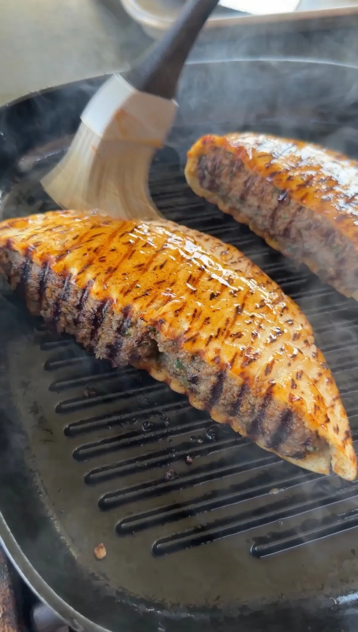 Stuffed pita arayes on a cast-iron skillet being brushed with smoked paprika oil, showing golden grill marks