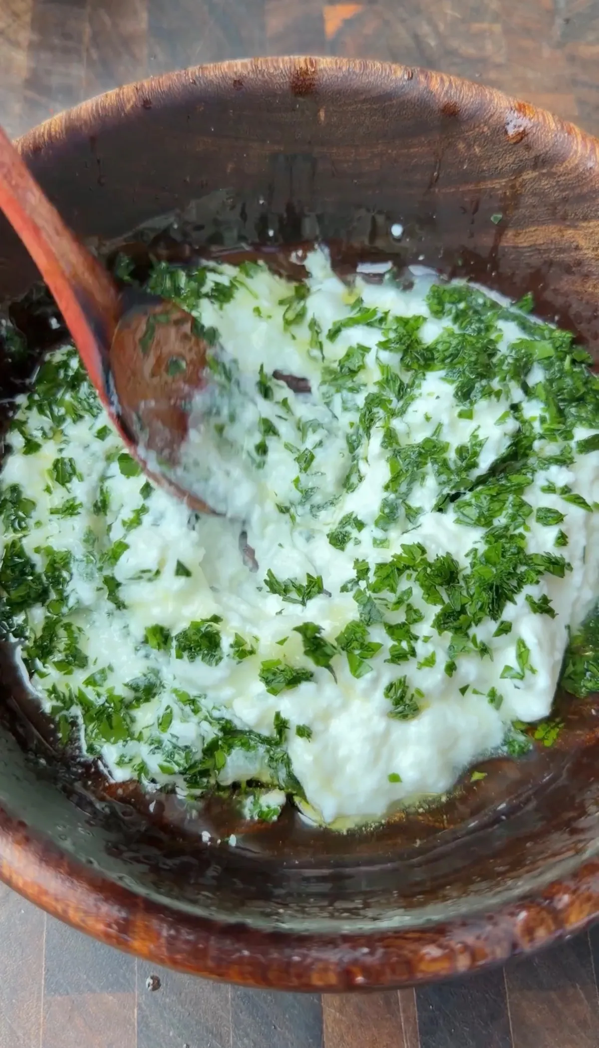 Greek yogurt dipping sauce with grated garlic, lemon juice, olive oil, and chopped fresh parsley in a wooden bowl