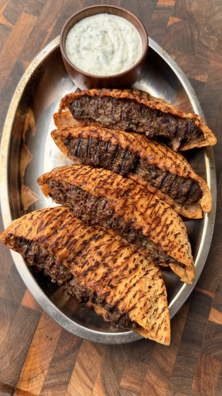 Arayes with grilled beef-stuffed pita halves on a metal platter served with garlic yogurt dipping sauce