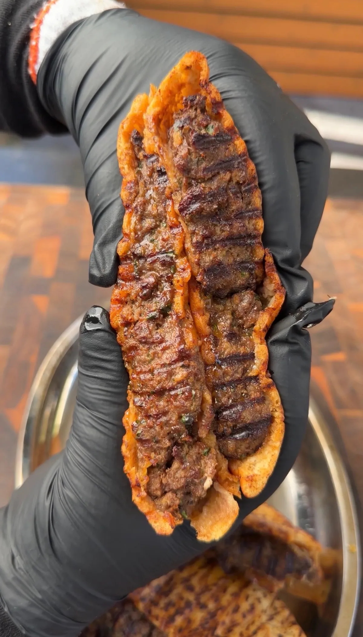 Hands in black gloves holding arayes with seared ground beef filling and smoked paprika-oiled pita crust