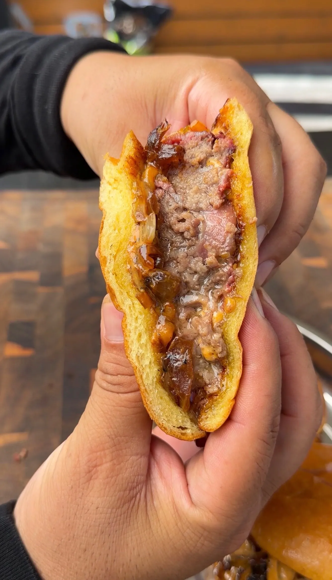 Hands holding open a bacon cheeseburger pinwheel showing juicy ground beef, caramelized onions, and crispy toasted bun
