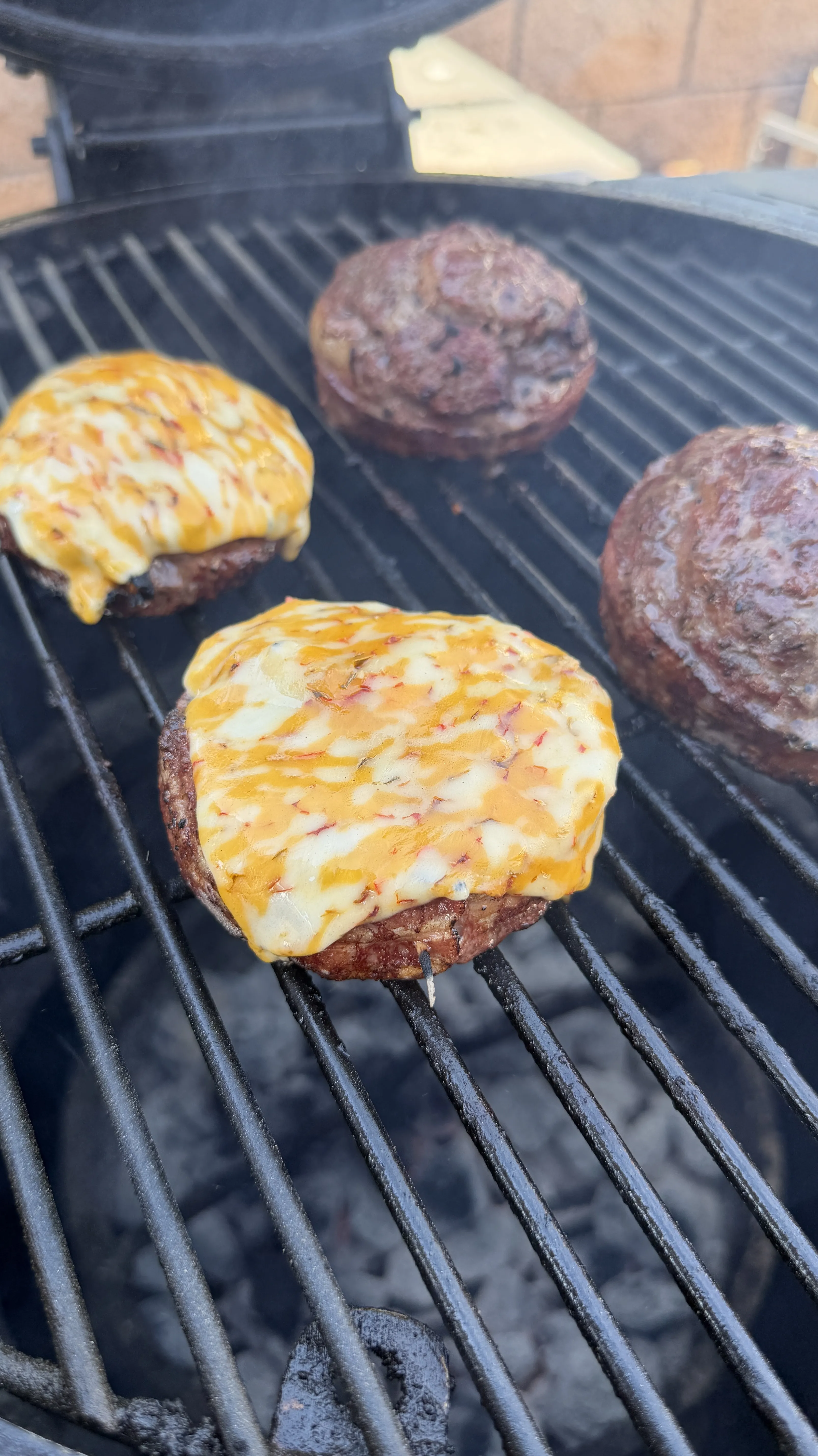 Bacon cheeseburger pinwheels on a charcoal grill, two topped with melted cheddar cheese