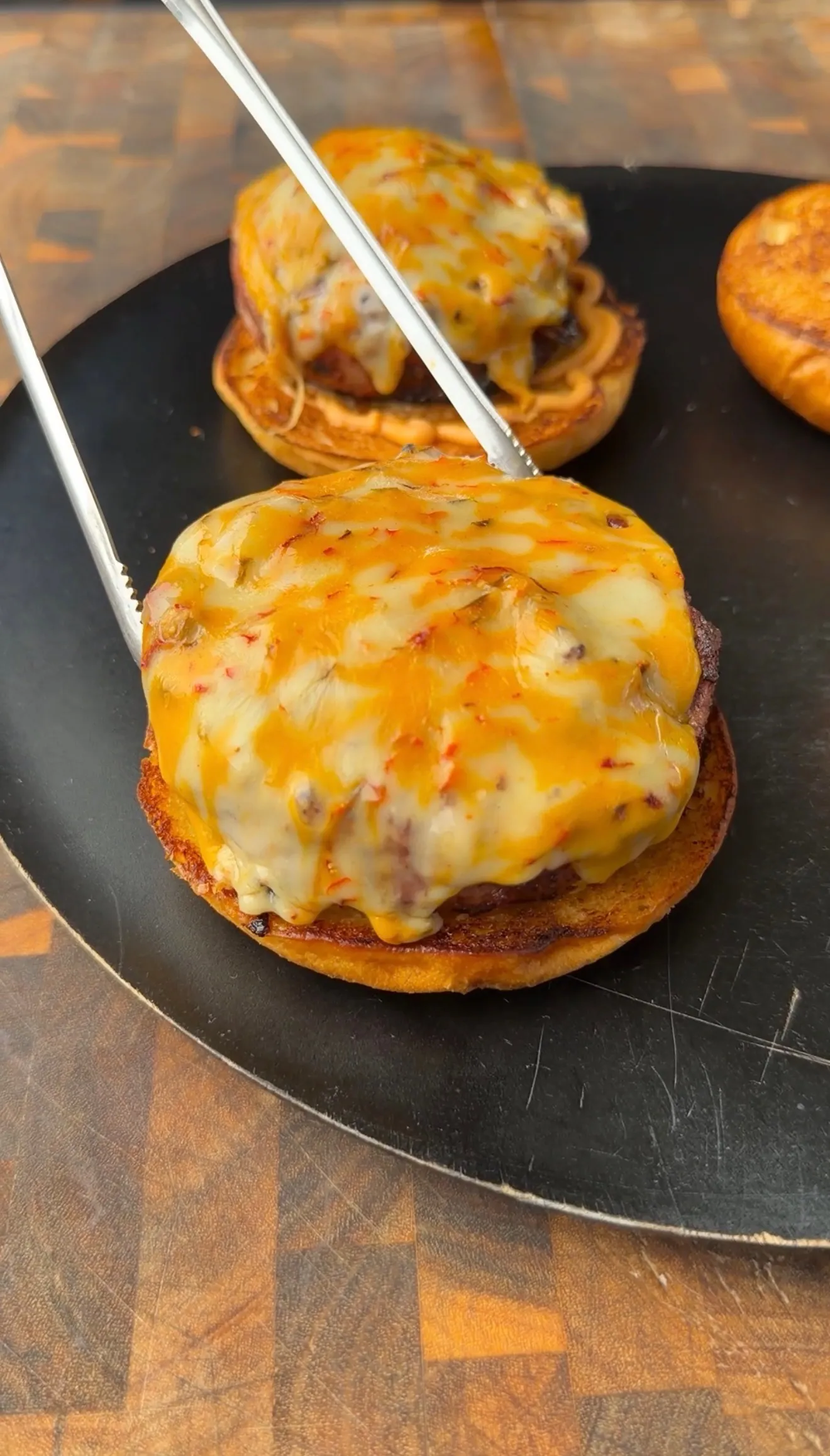 Bacon cheeseburger pinwheels with bubbling melted cheddar cheese on toasted buns, held with tongs on a black plate