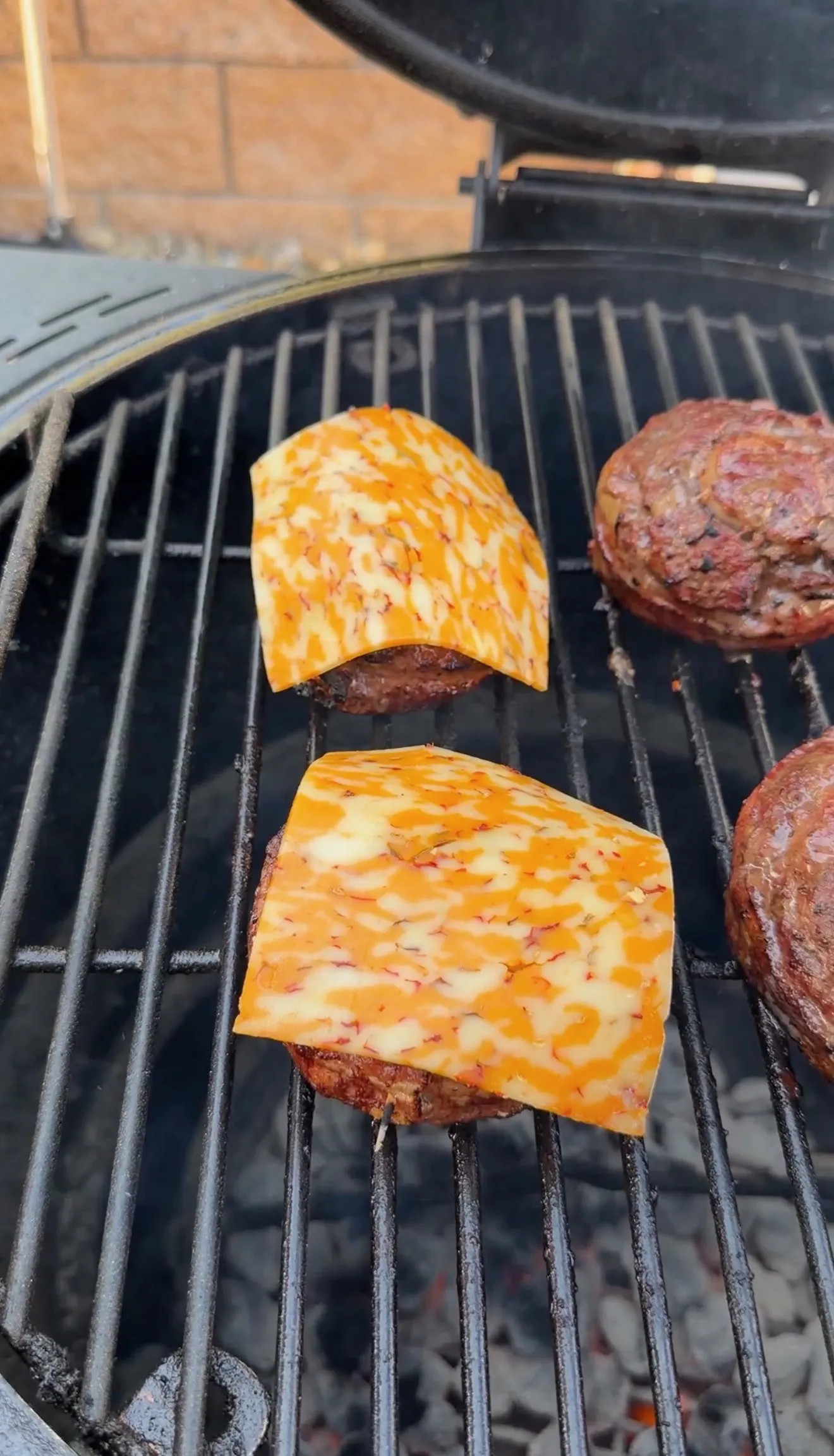 Bacon cheeseburger pinwheels topped with melting pepper jack cheese slices cooking on a charcoal grill