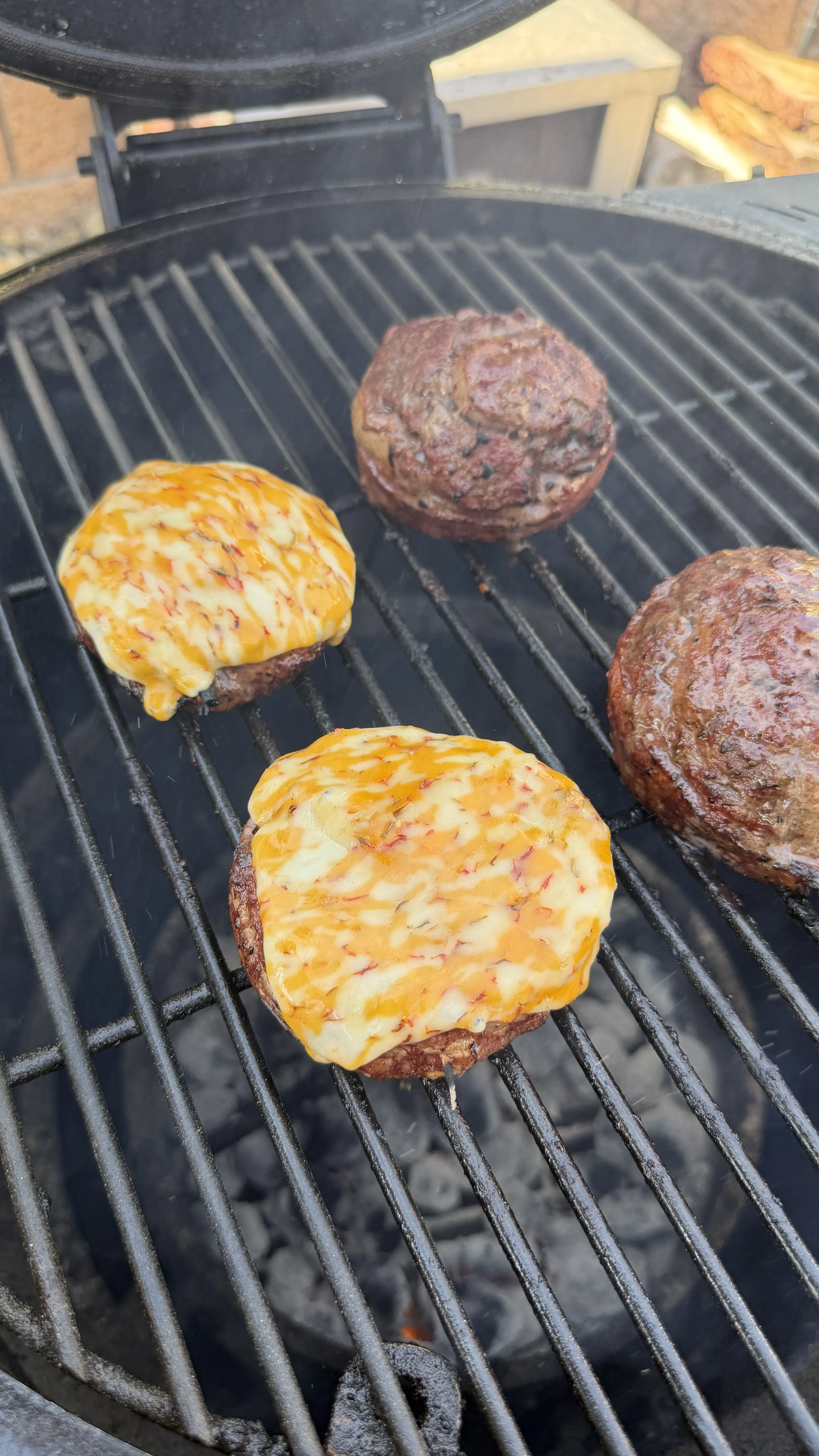 Four bacon cheeseburger pinwheels on a charcoal grill, two topped with melted cheddar cheese