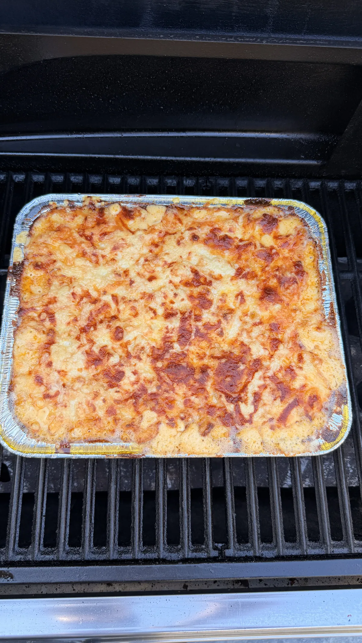 Creamy layered baked mac and cheese with golden, bubbly mozzarella and Colby Jack crust in foil pan on grill