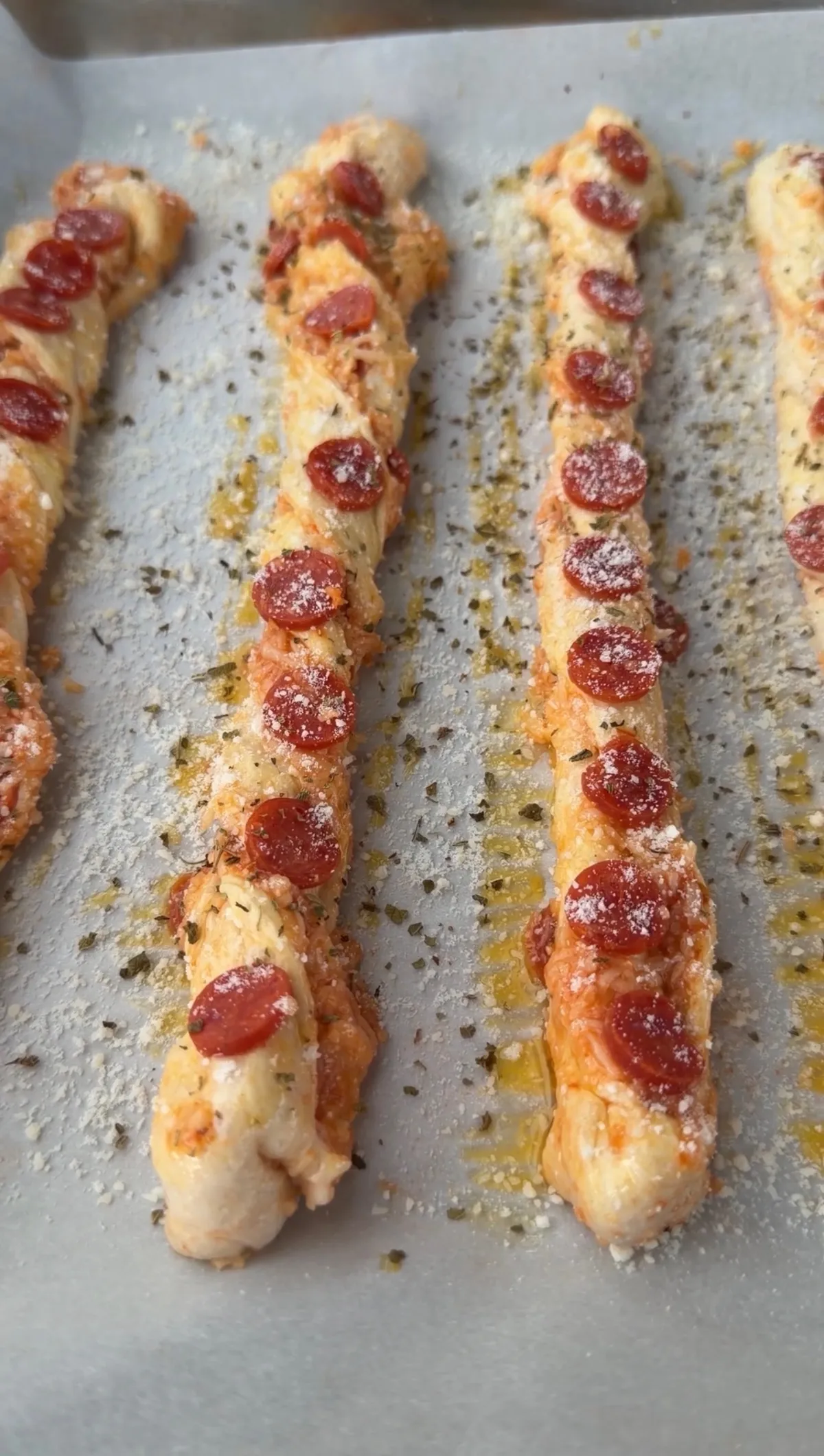 Golden baked pepperoni pizza twists topped with mini pepperonis, Parmesan, and oregano on a parchment-lined baking sheet